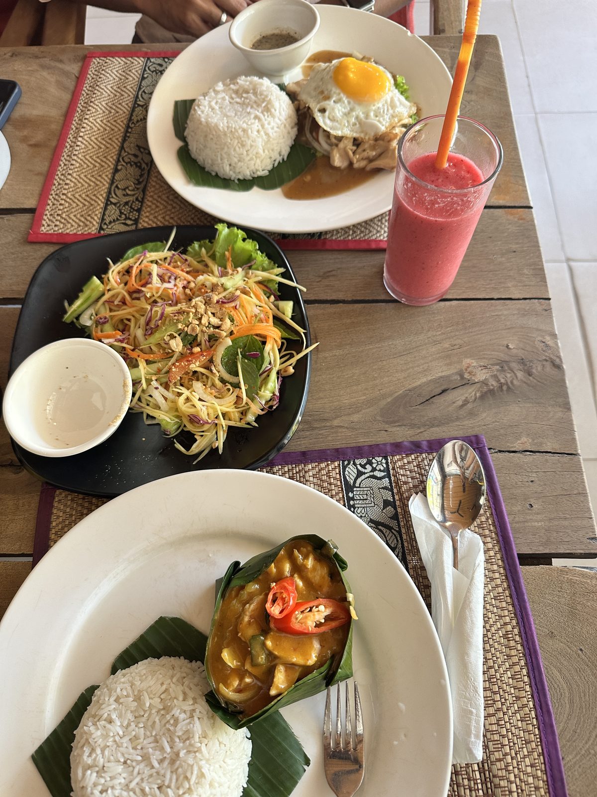 A Khmer lunch of fish amok in banana leaf, green papaya salad, chicken with fried egg and rice, and a watermelon smoothie