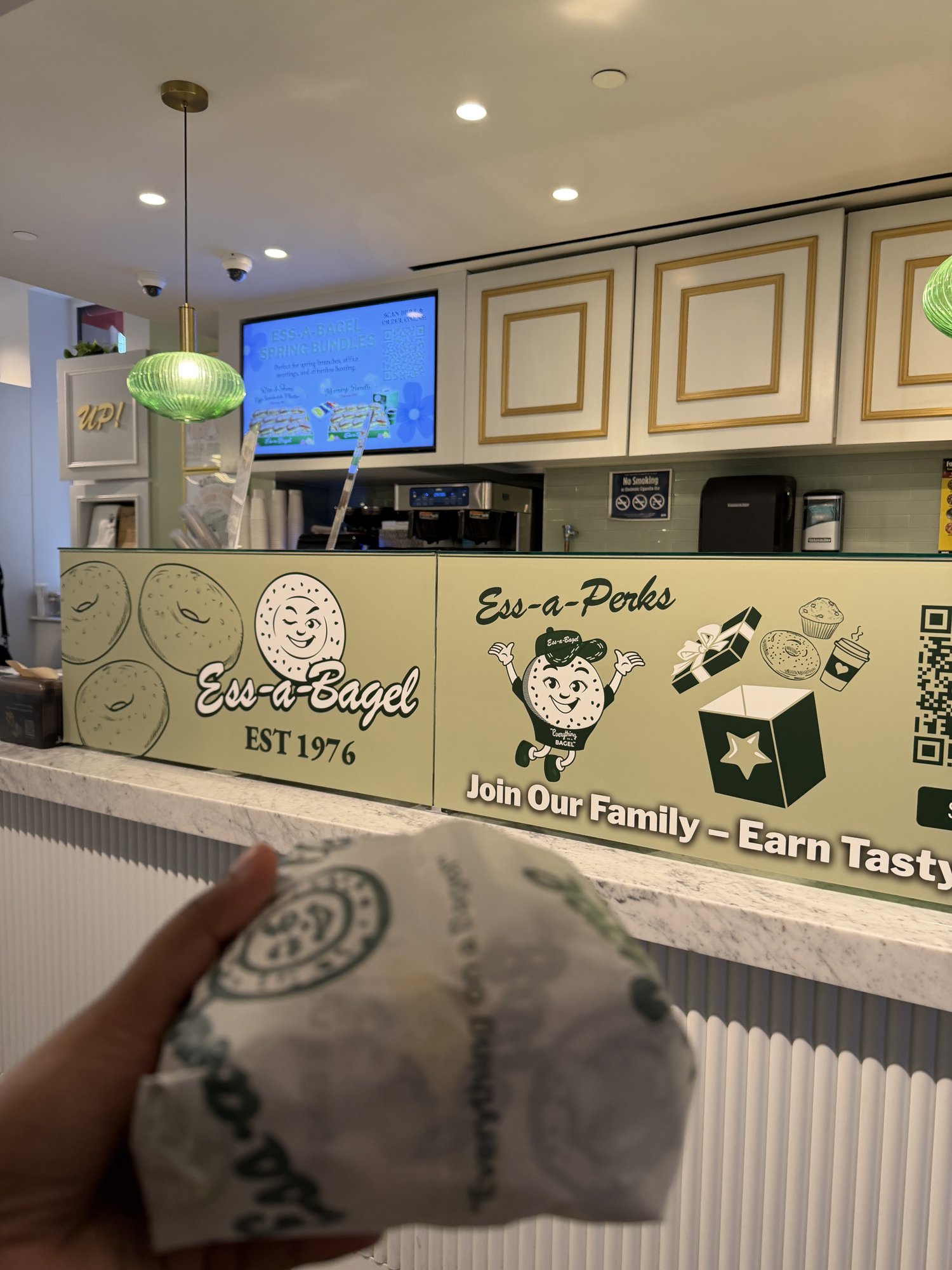 A wrapped bagel held up in front of the Ess-a-Bagel counter in New York