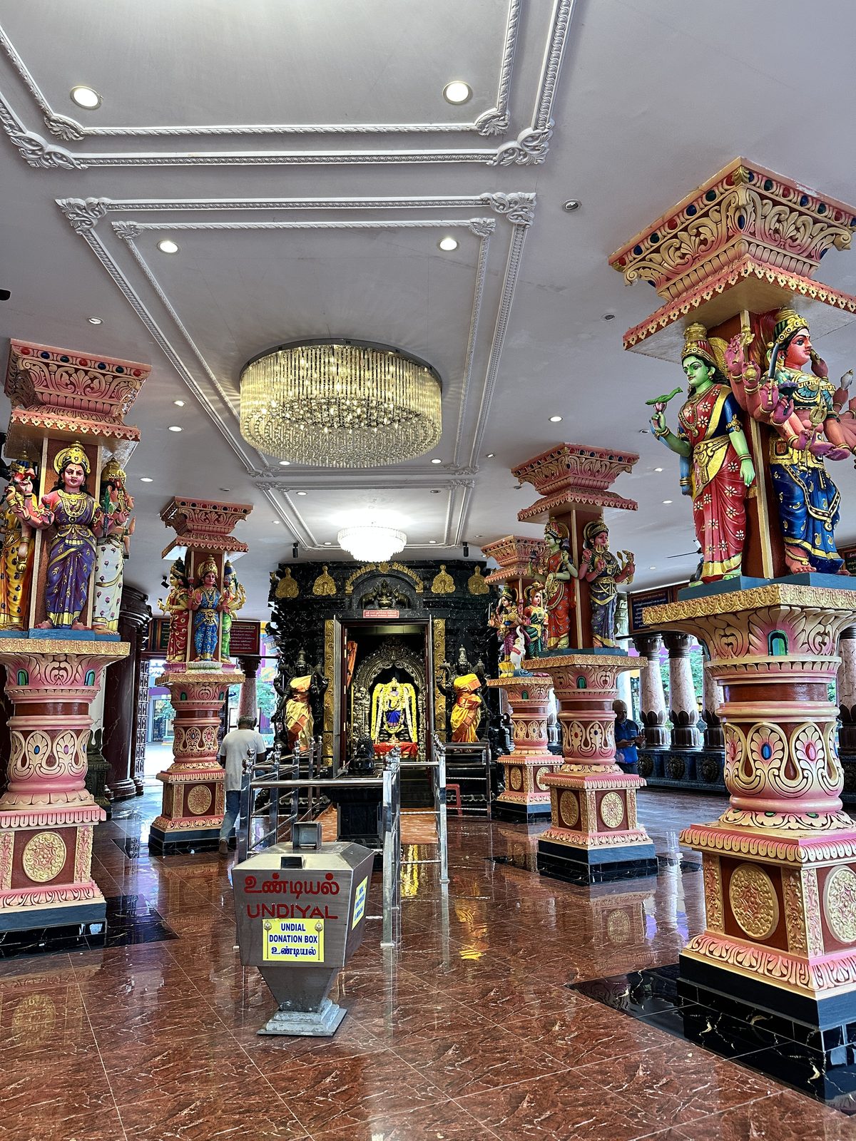 The interior of the temple at Batu Caves with painted pillars, deity figures and a black marble shrine