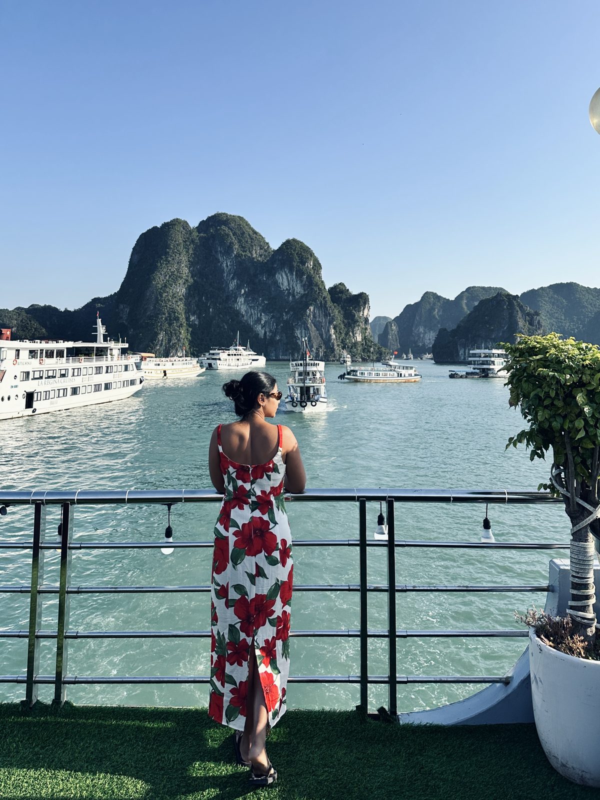A woman looking out over Ha Long Bay from a cruise boat deck, karst islands and half a dozen other boats ahead