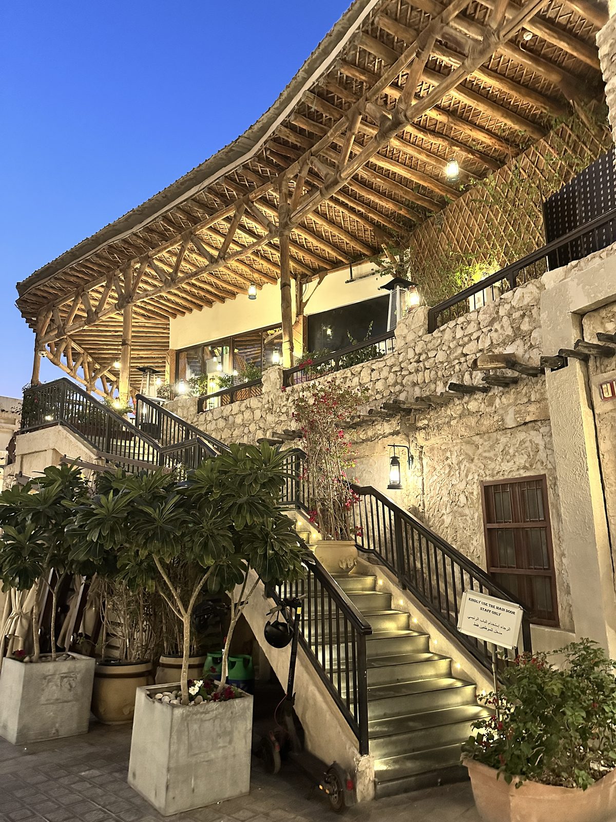Souq Waqif at blue hour, restored mud-brick buildings with exposed wooden roof beams and lit lanterns above a stone staircase