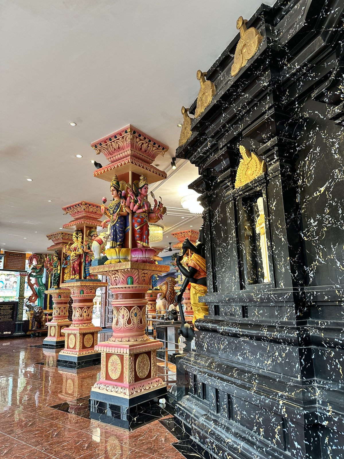 Carved and painted temple pillars with deity figures, reflected in a polished marble floor