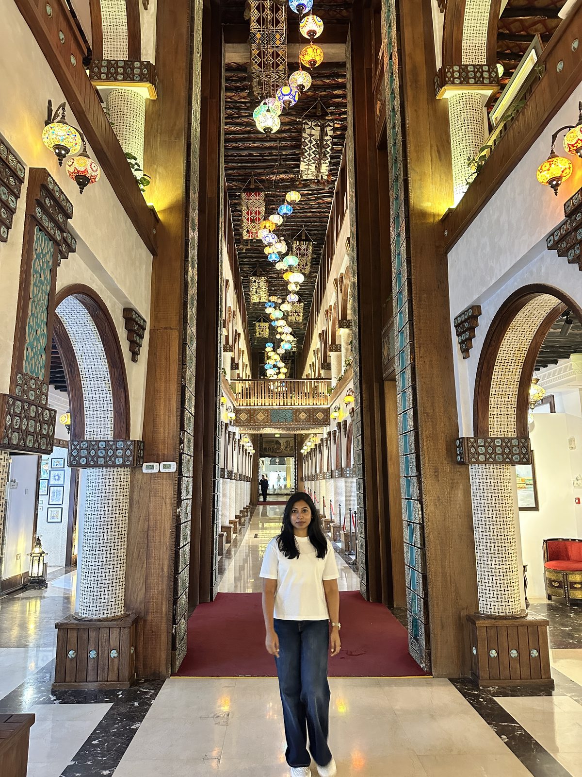 A long high corridor lined with carved wooden columns and dozens of coloured hanging lanterns