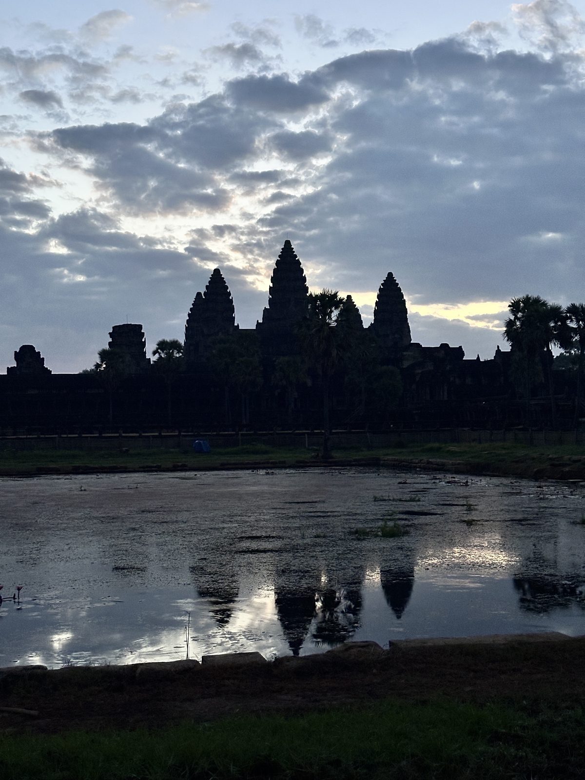 Angkor Wat's five towers in silhouette against a dawn sky, reflected in the still water of the pool