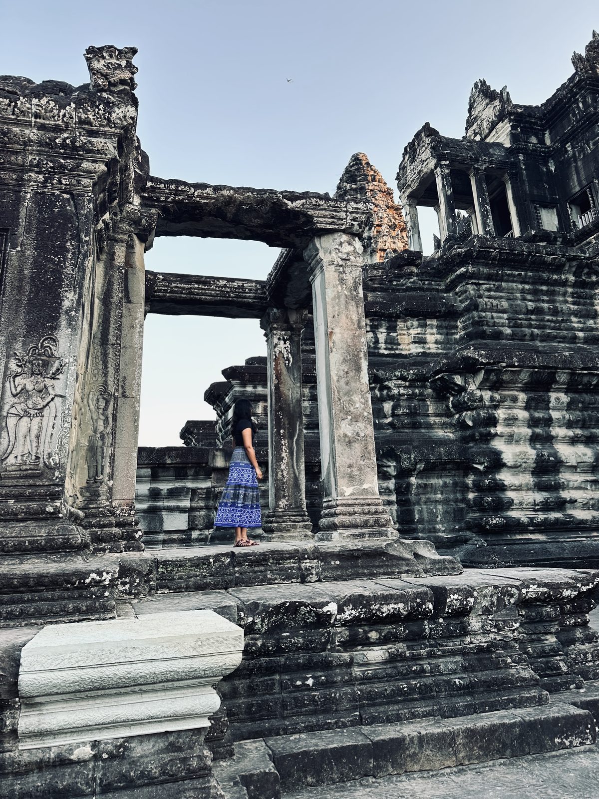 A woman in a long blue patterned skirt standing among the columns and galleries of Angkor Wat's upper level