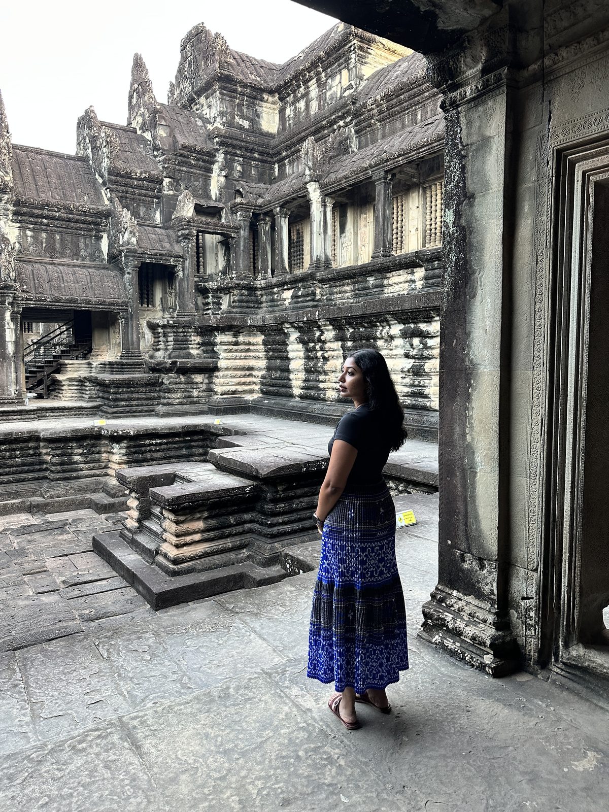 A woman standing in the inner courtyard of Angkor Wat, surrounded by carved galleries and steep stone stairs