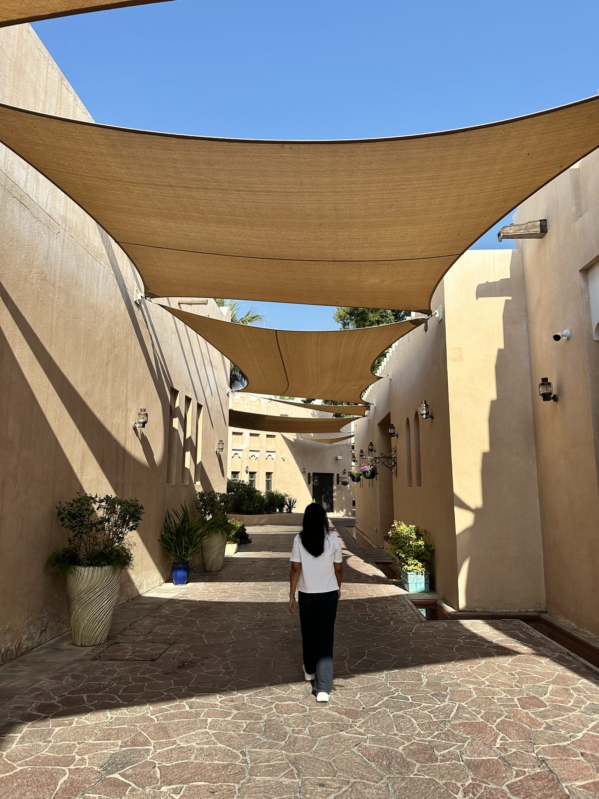 A woman walking down a shaded sand-coloured alleyway hung with overlapping fabric shade sails