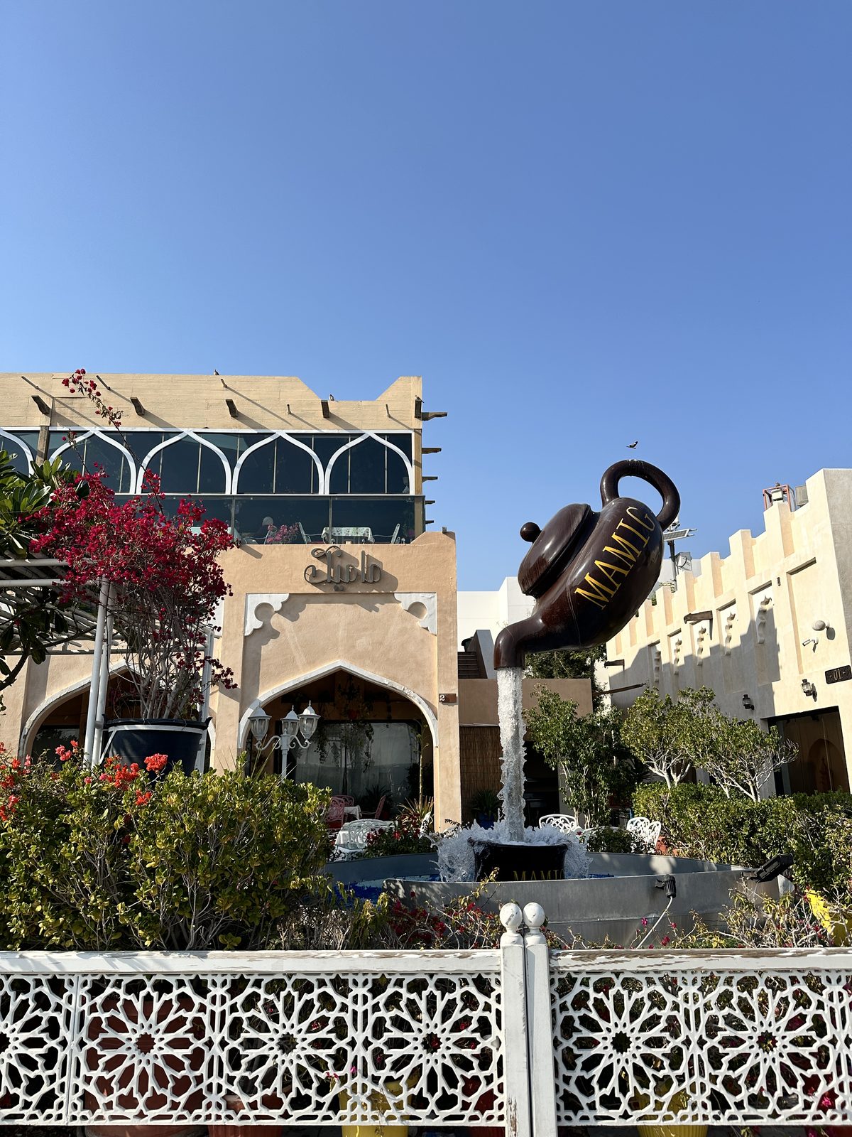 A restaurant courtyard with a giant floating teapot sculpture pouring water into a fountain below