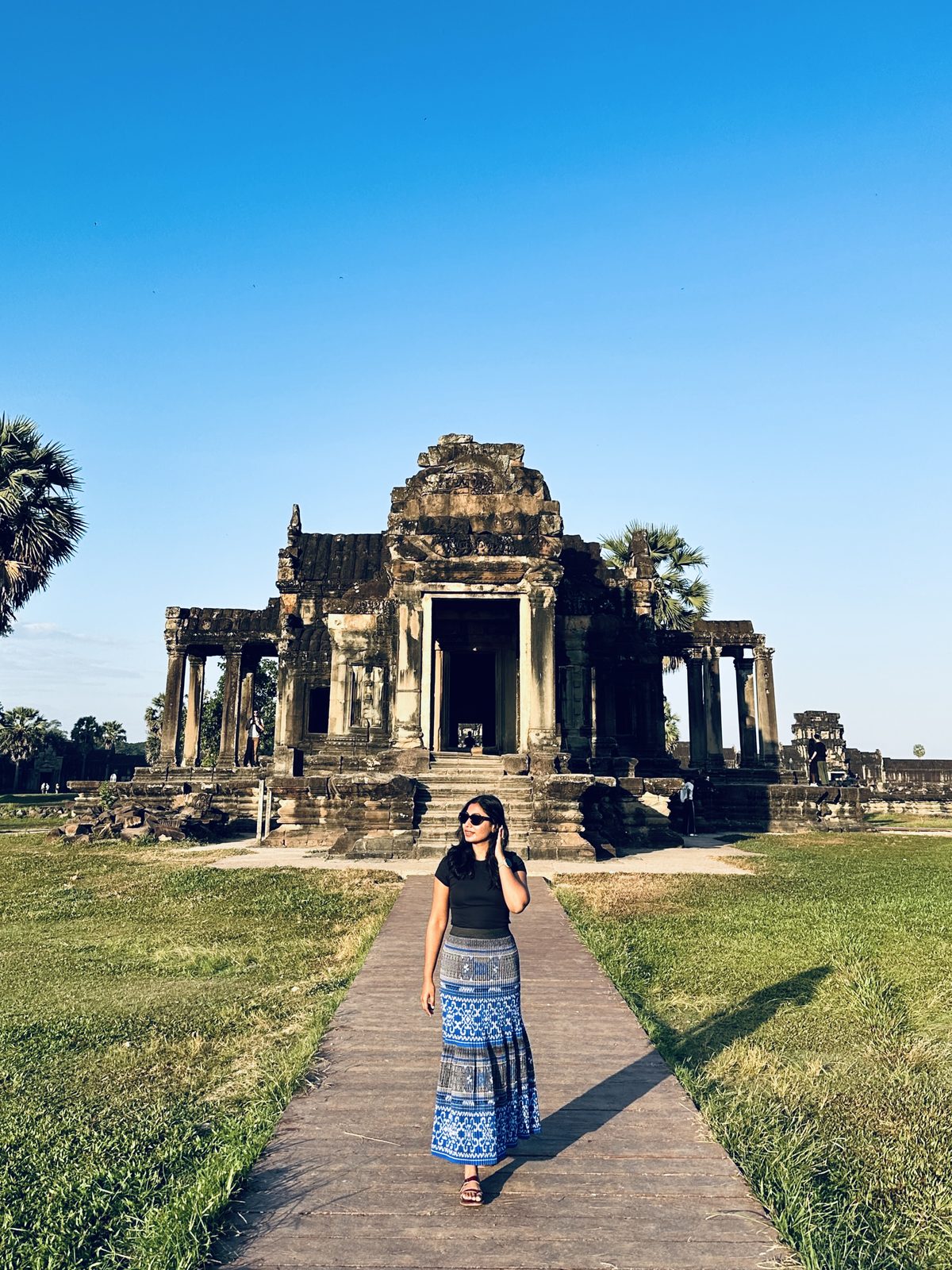 A woman walking a raised stone path toward one of Angkor Wat's library buildings under a deep blue sky