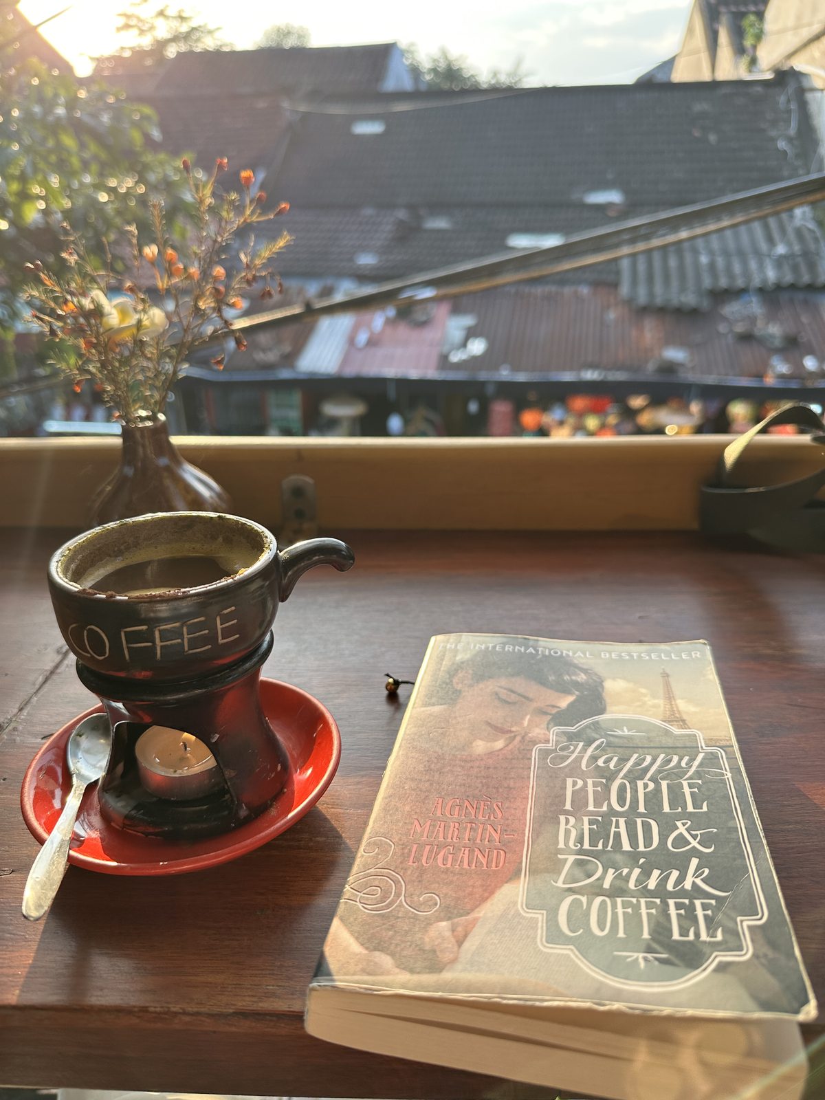 An egg coffee on its warmer beside a paperback copy of Happy People Read and Drink Coffee