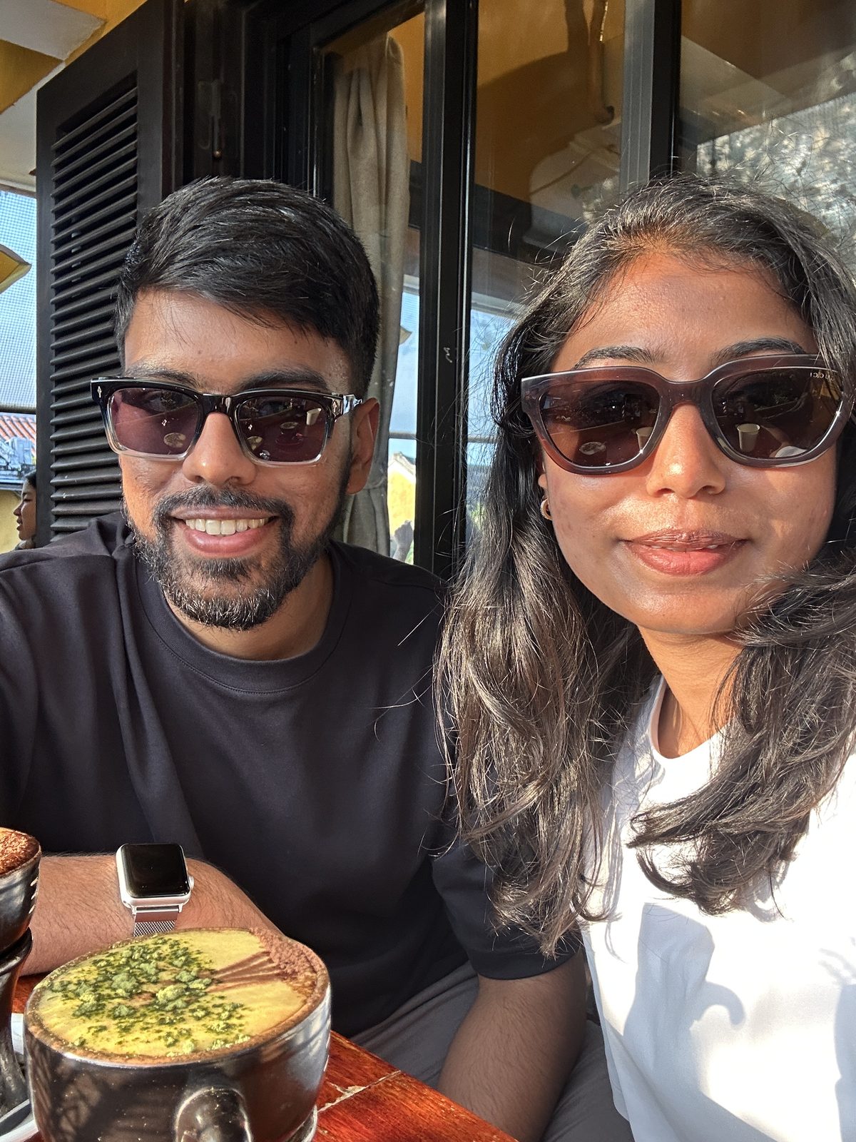 A couple in sunglasses at a Hoi An cafe table with egg coffee in front of them