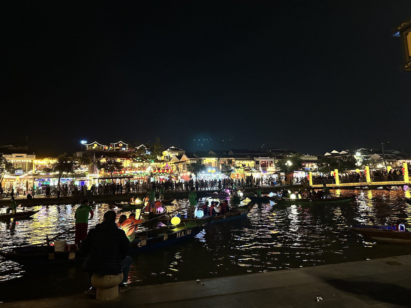 The Hoi An riverfront at night, crowded with lantern boats and the lit ancient town behind