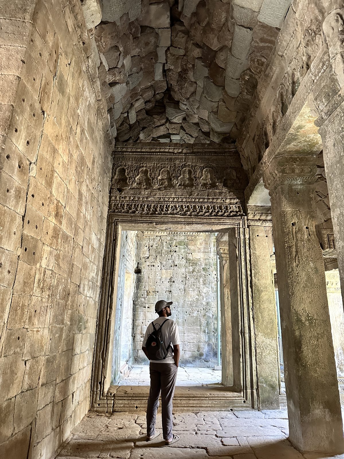 A man standing in a carved stone corridor at Ta Prohm, looking up at a decorated lintel