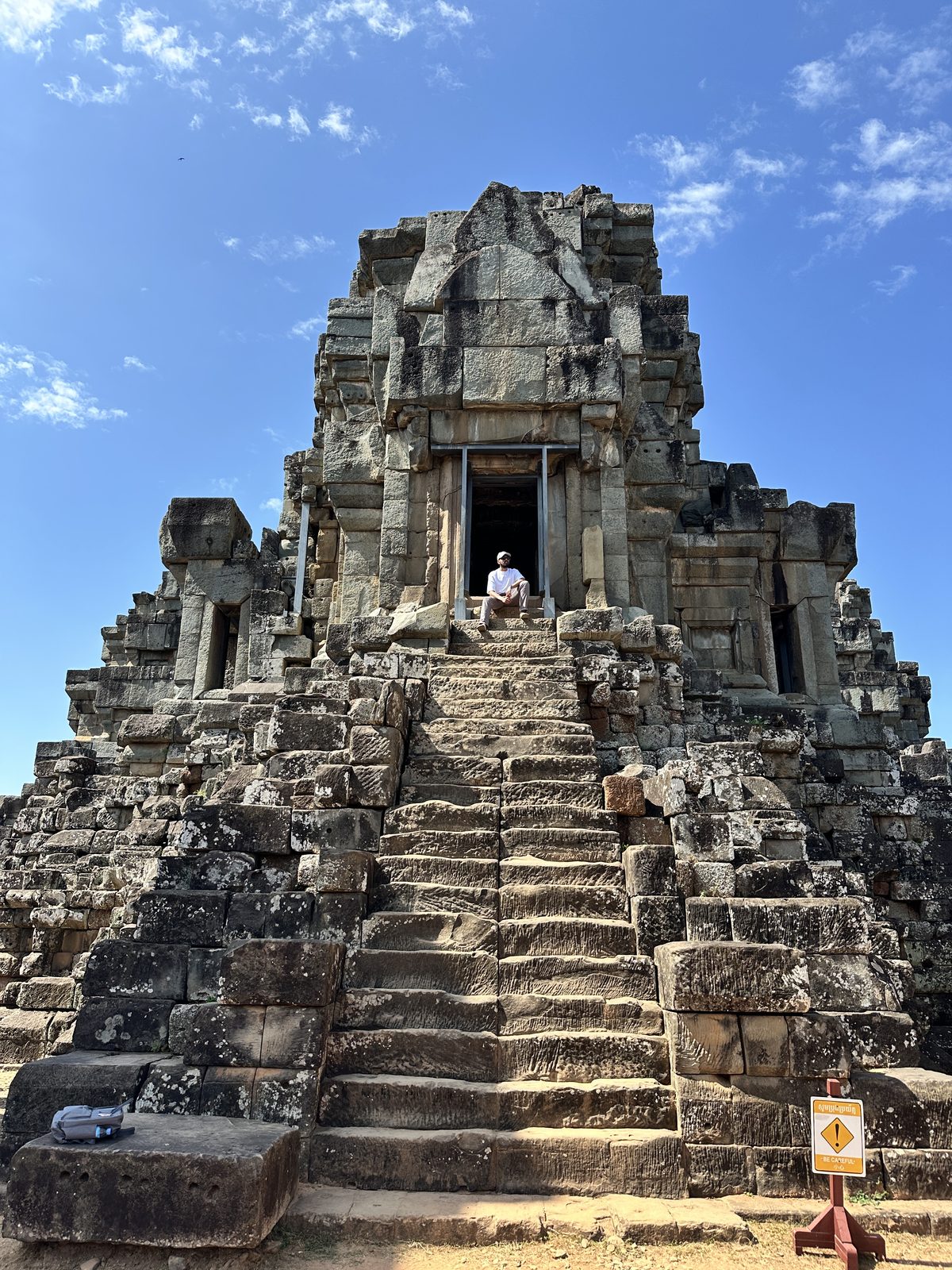 A man sitting at the top of the very steep central stairs of Ta Keo, a stepped pyramid temple