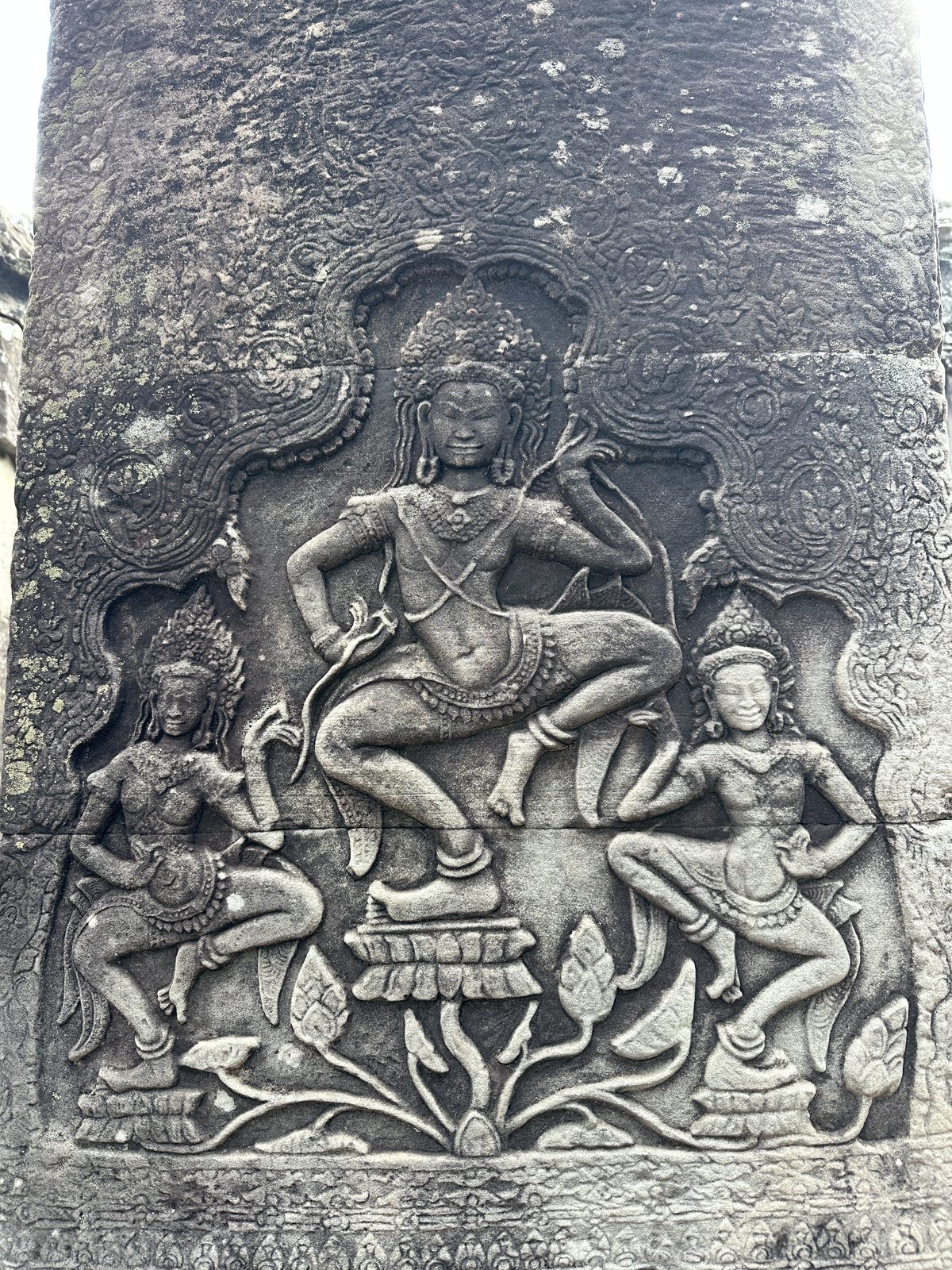A carved stone relief of a dancing celestial figure on a lotus, flanked by two smaller dancing attendants