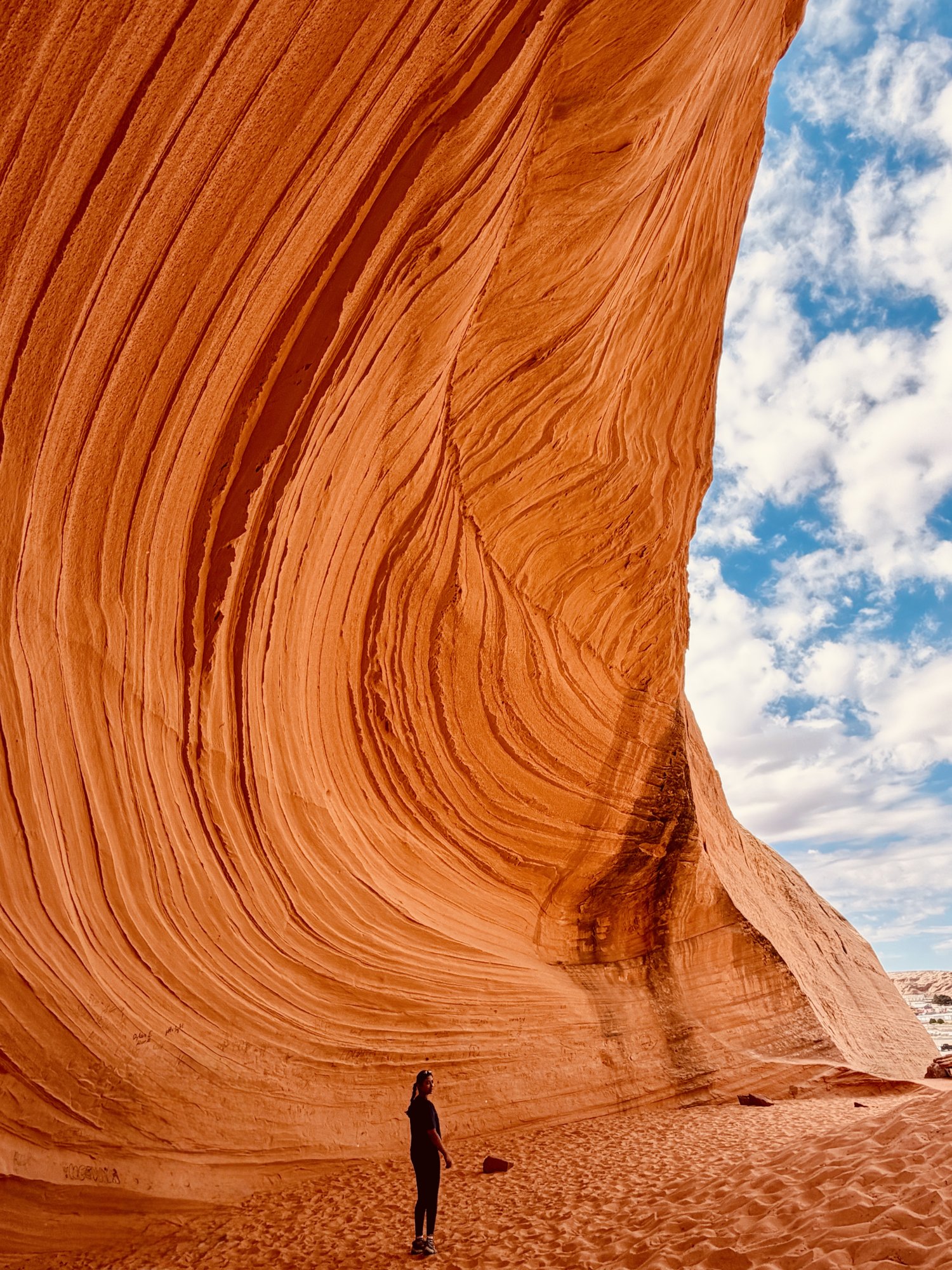 A person standing beneath the huge curved striped sandstone wall of the New Wave near Page, Arizona