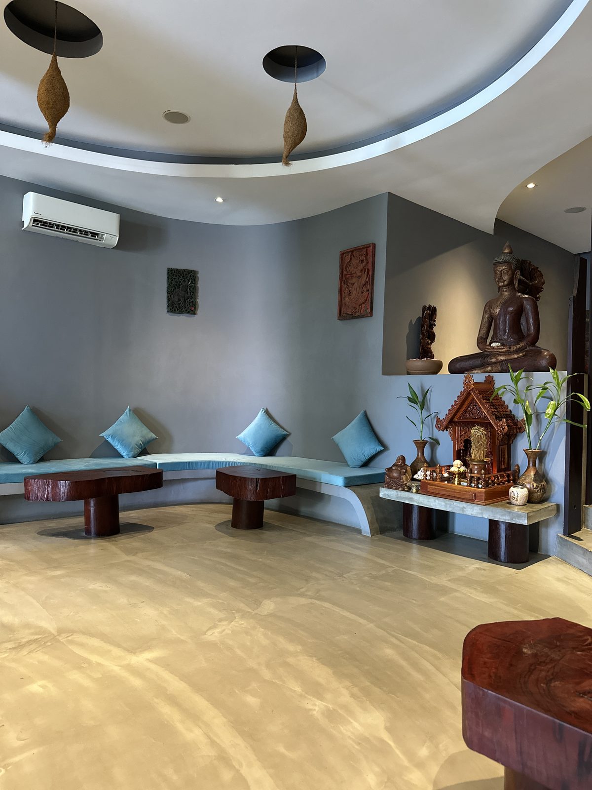 The reception room of a spa in Siem Reap, with grey walls, blue cushioned benches, a wooden Buddha and a spirit house