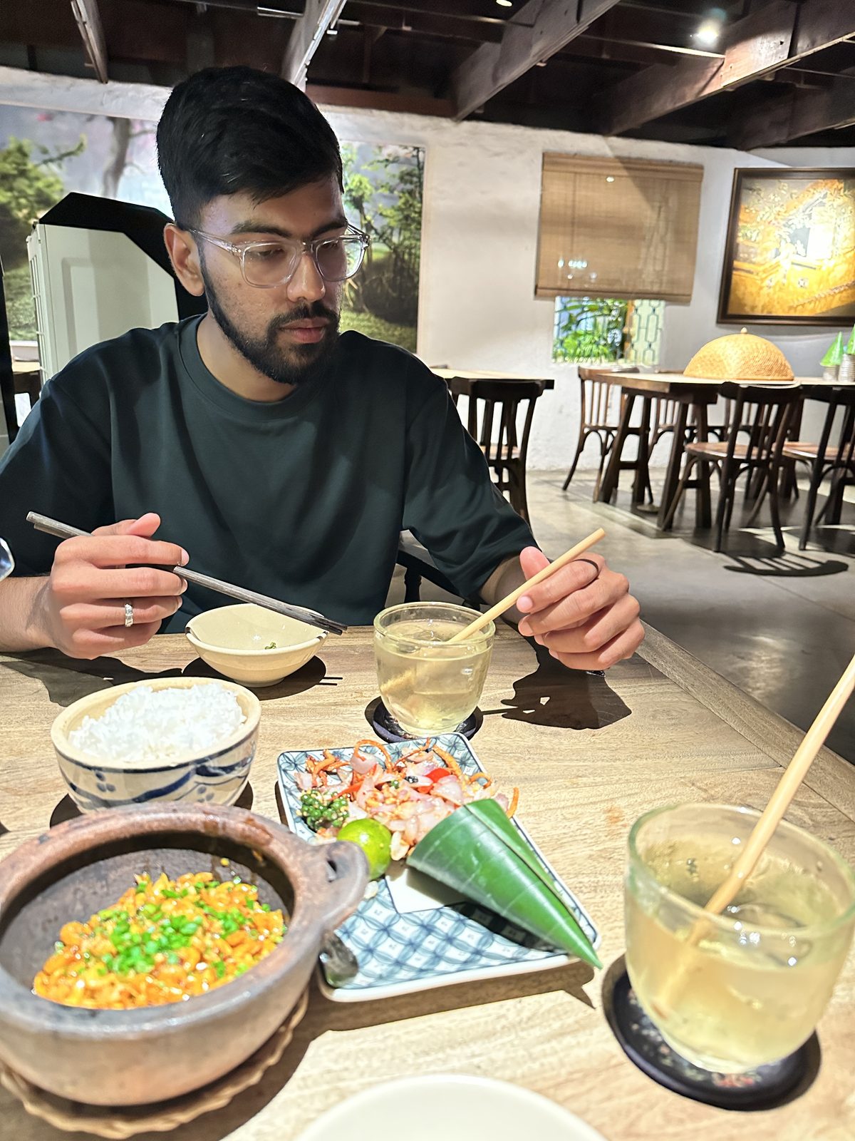 A man eating at a wooden table, with a clay pot dish, a salad plate and iced tea