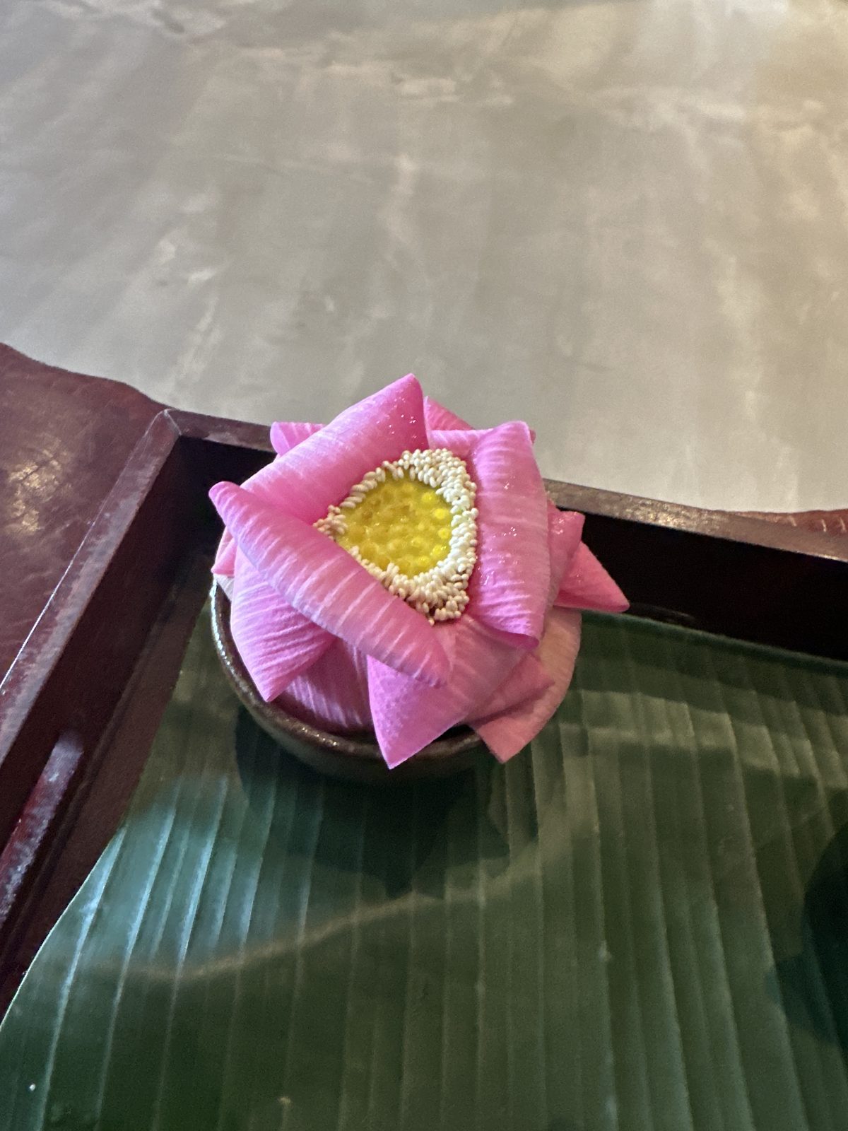A pink lotus flower folded open around a small dish, sitting on a banana leaf tray