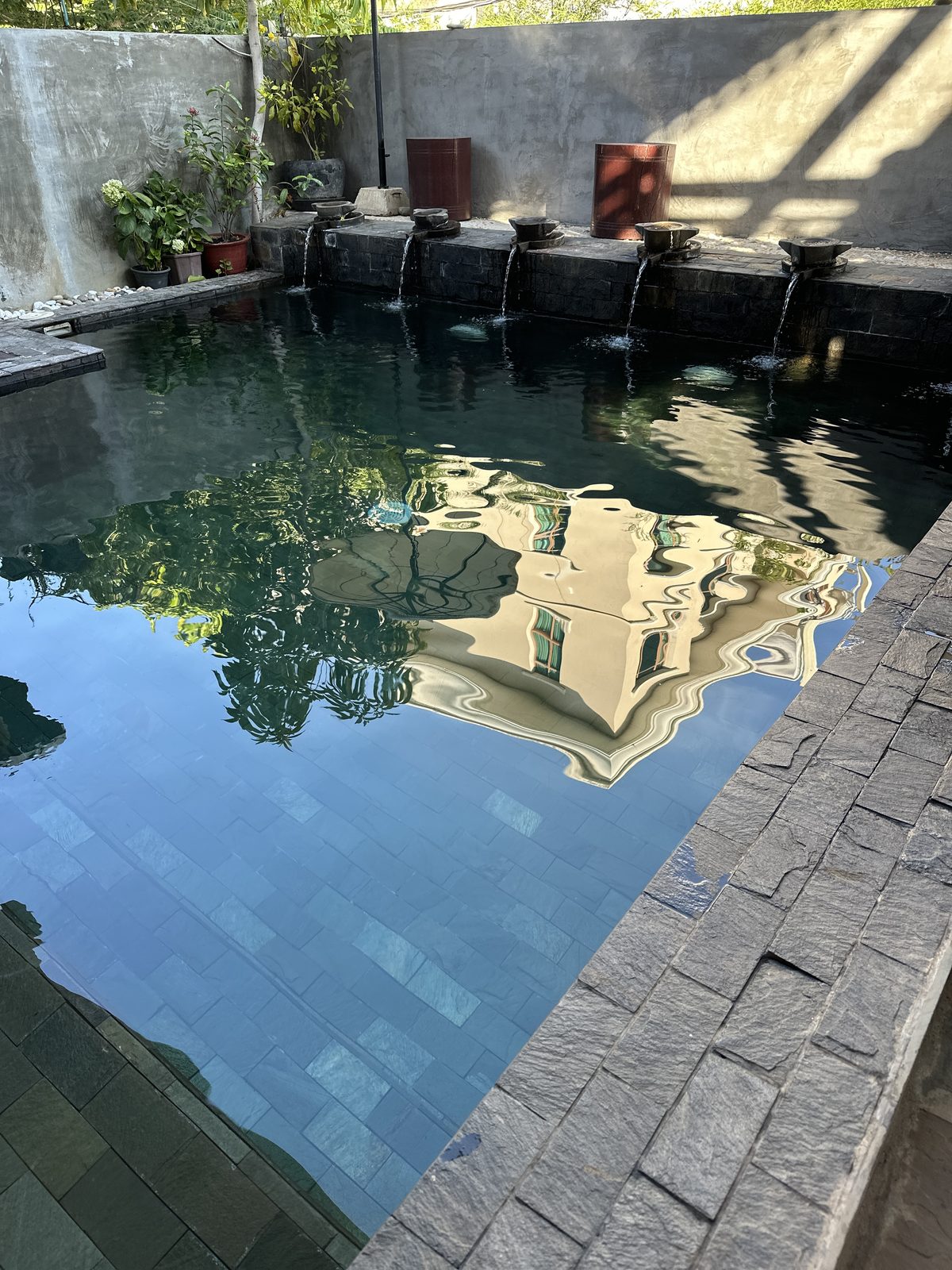 A small swimming pool with stone water spouts, the building reflected in the surface