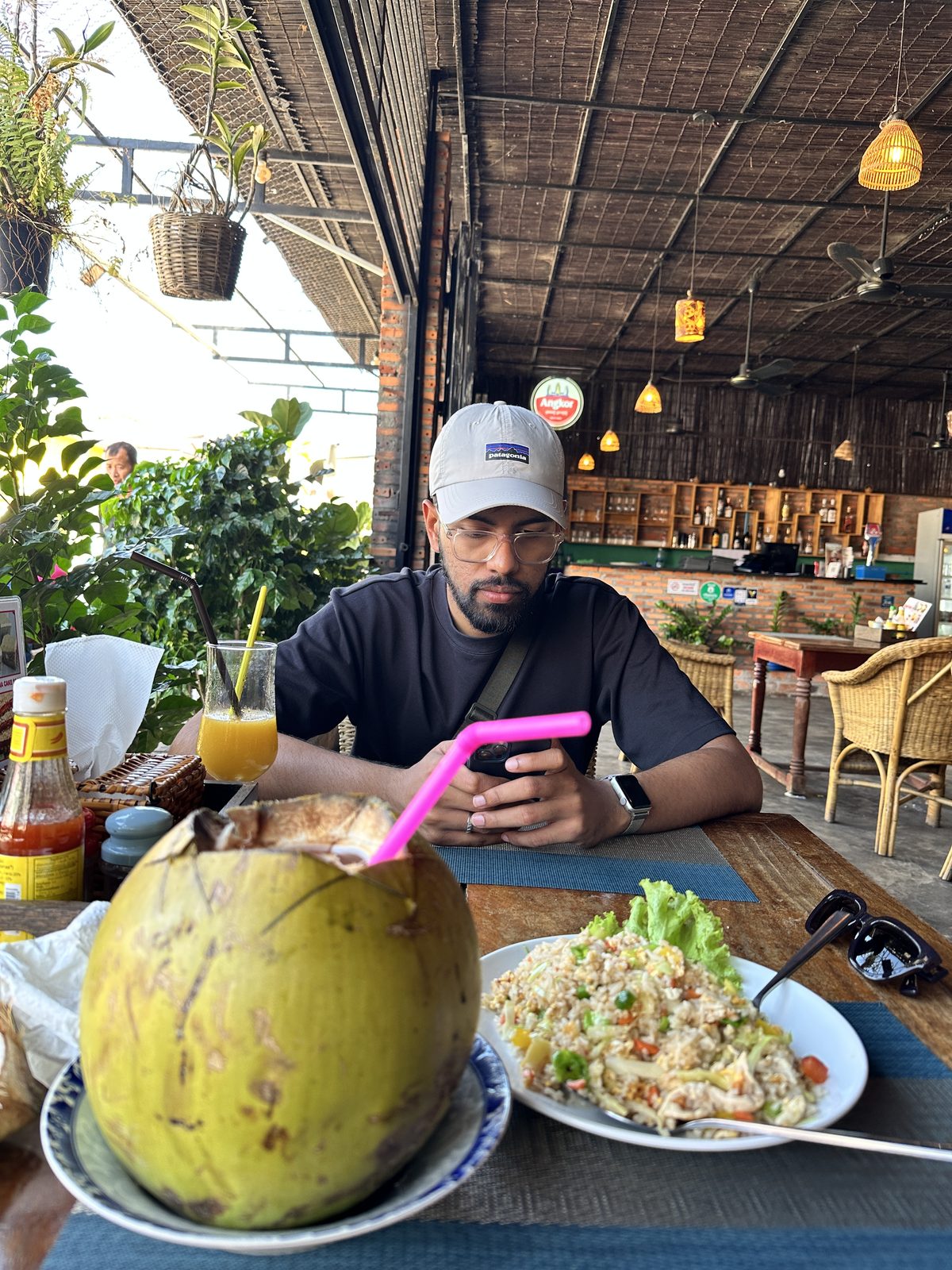 A lunch of fried rice and a whole young coconut with a pink straw, at an open-sided bamboo restaurant
