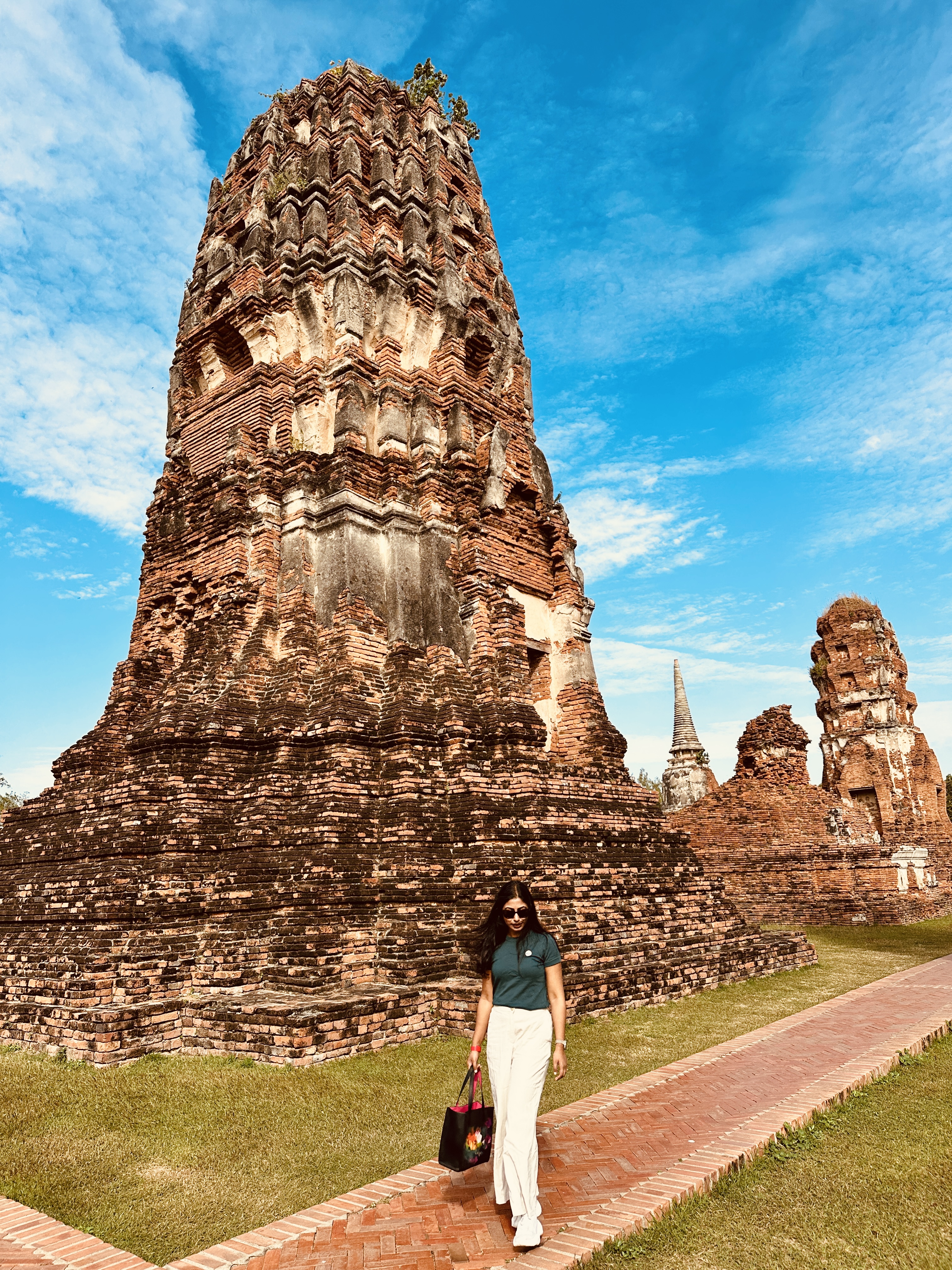 A woman standing at the base of a large brick prang at Ayutthaya under a blue sky