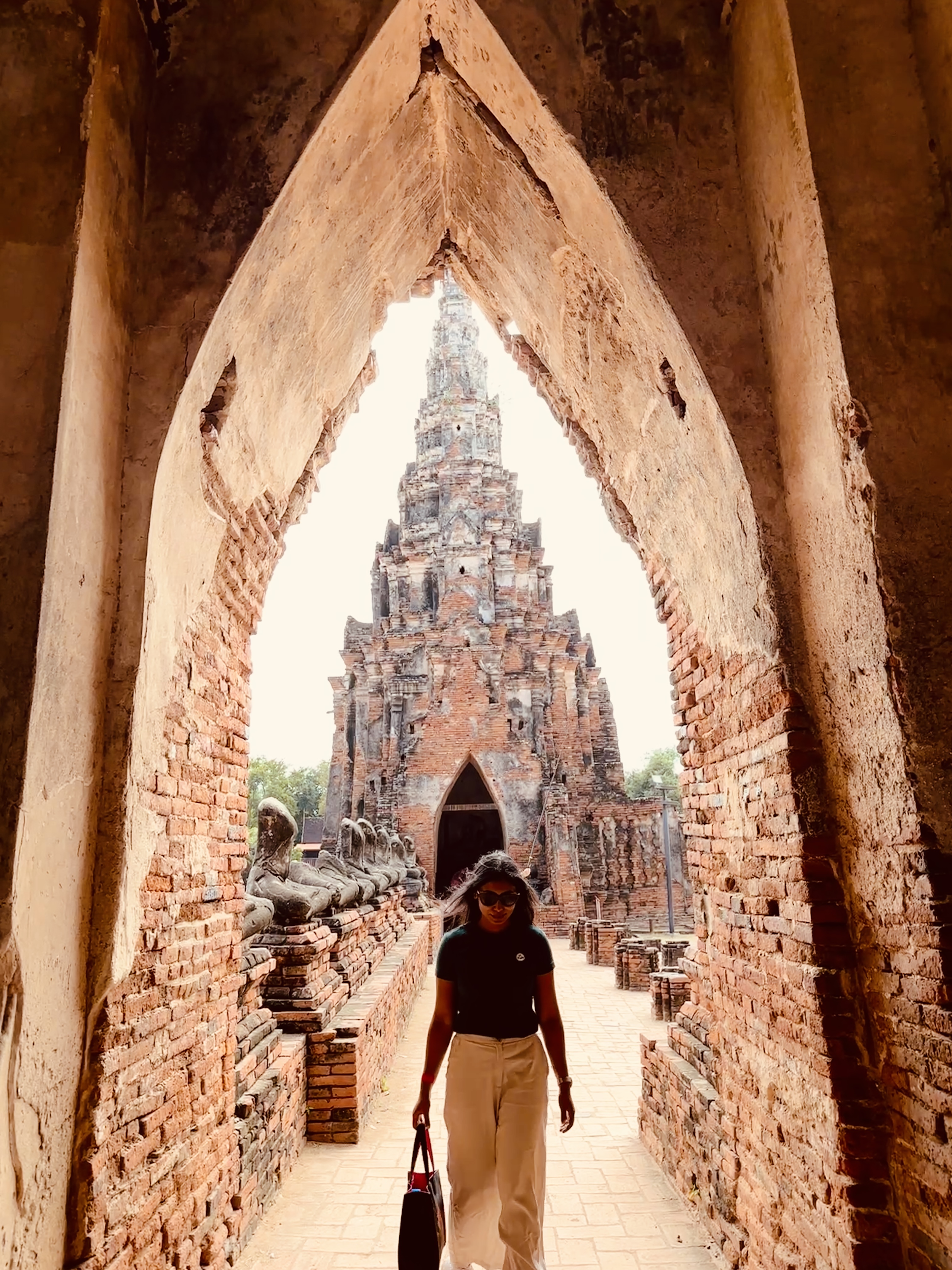 A woman walking through a long brick corridor at Ayutthaya with a prang ahead