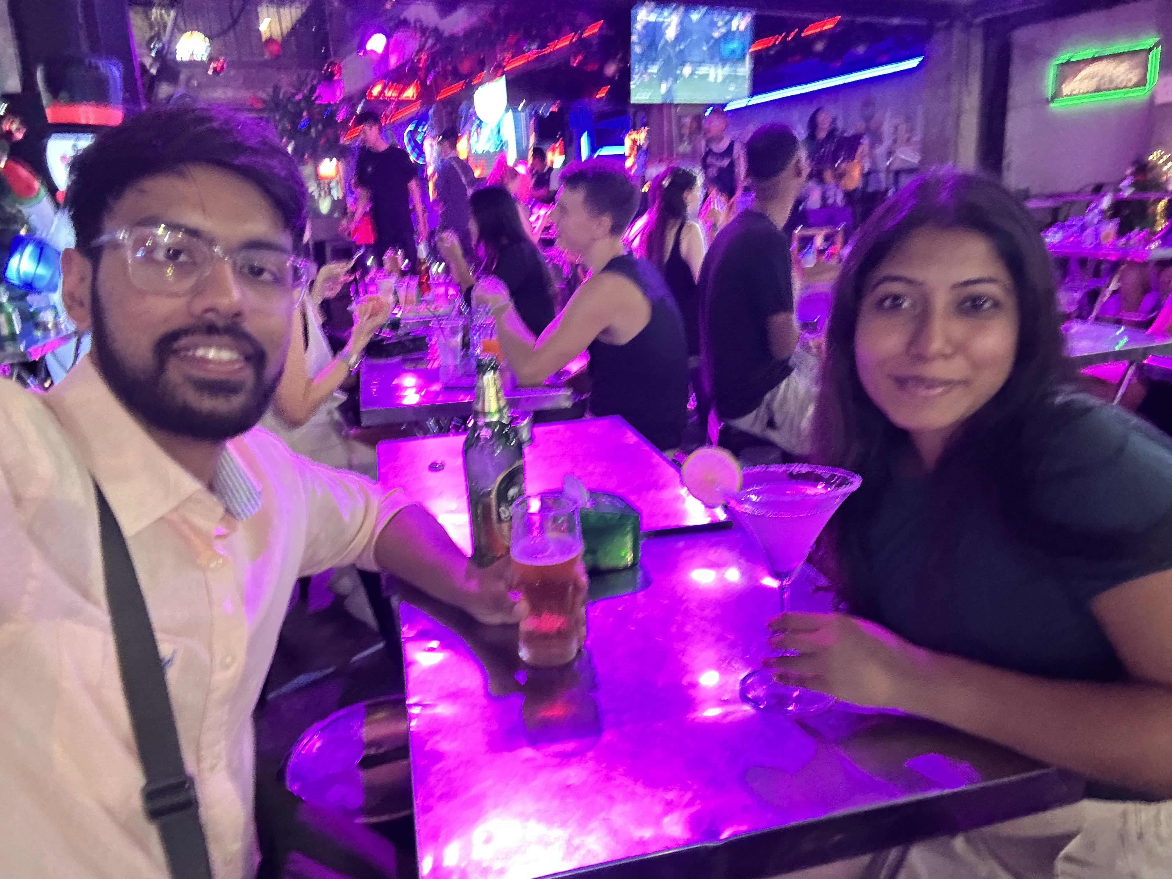 Two people at a neon-lit bar in Bangkok with brightly coloured cocktails