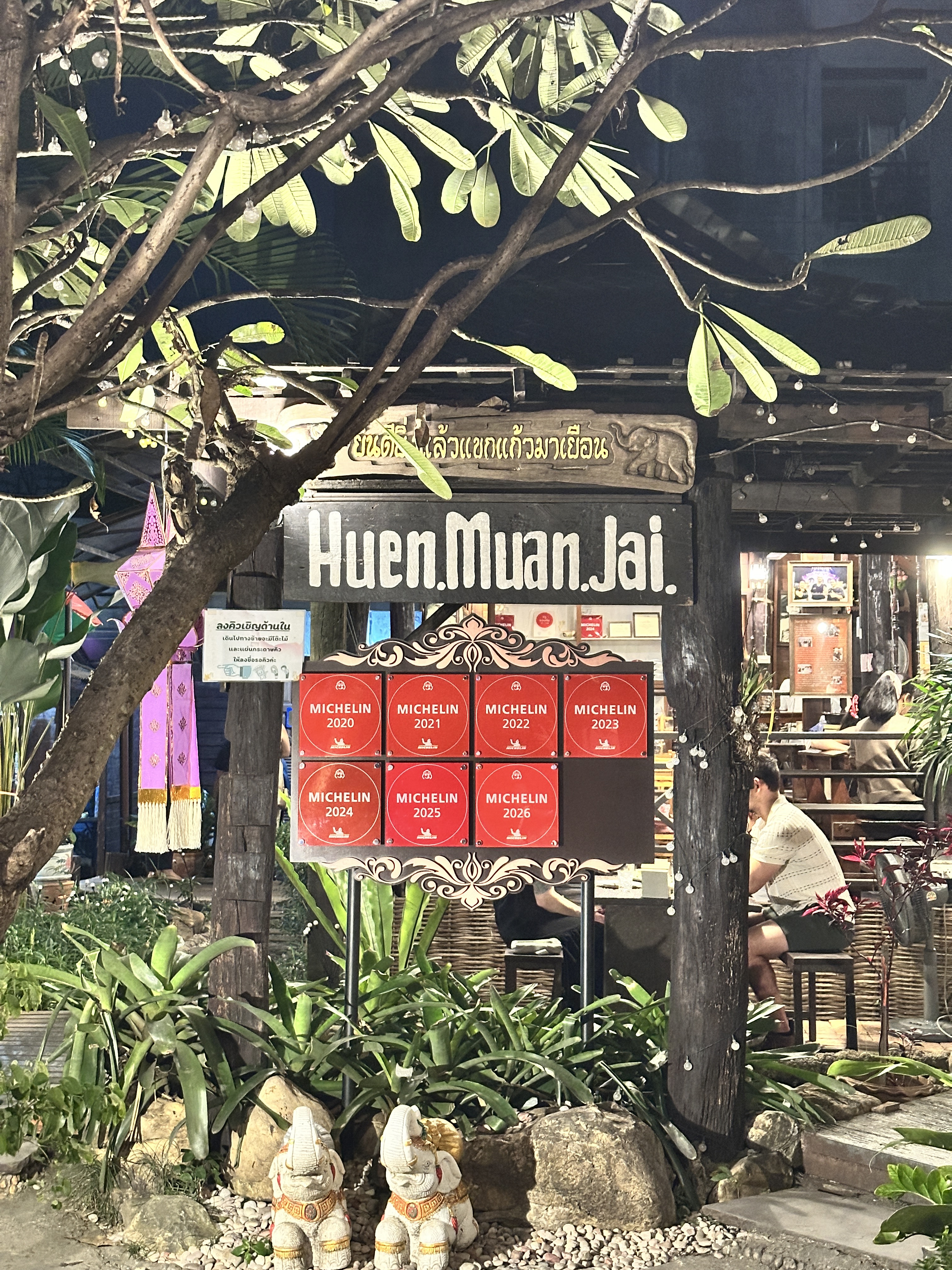 The entrance to Huen Muan Jai in Chiang Mai at night with seven red Michelin plaques mounted by the gate