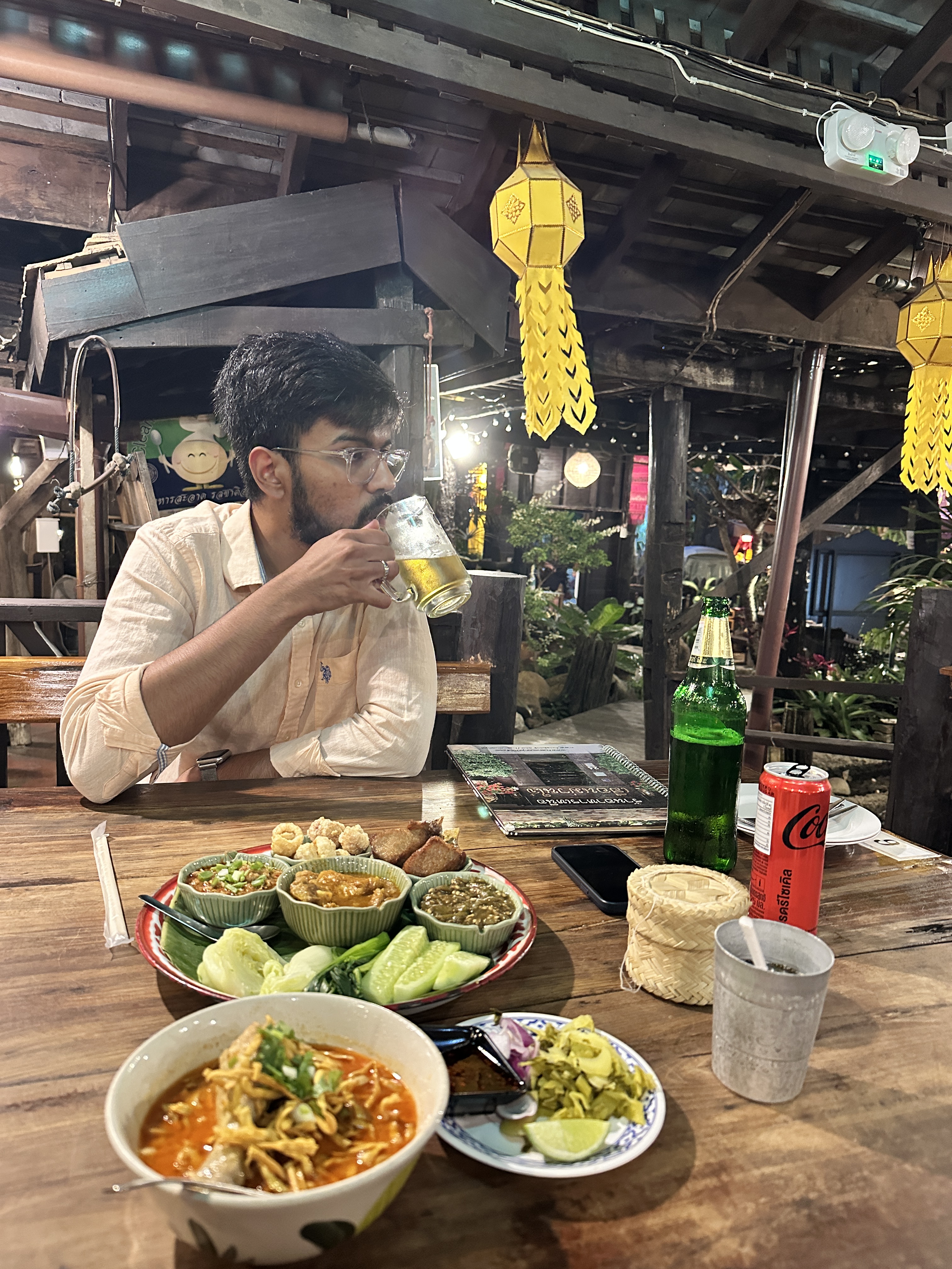 A man drinking a beer at a table spread with northern Thai dishes including khao soi at Huen Muan Jai