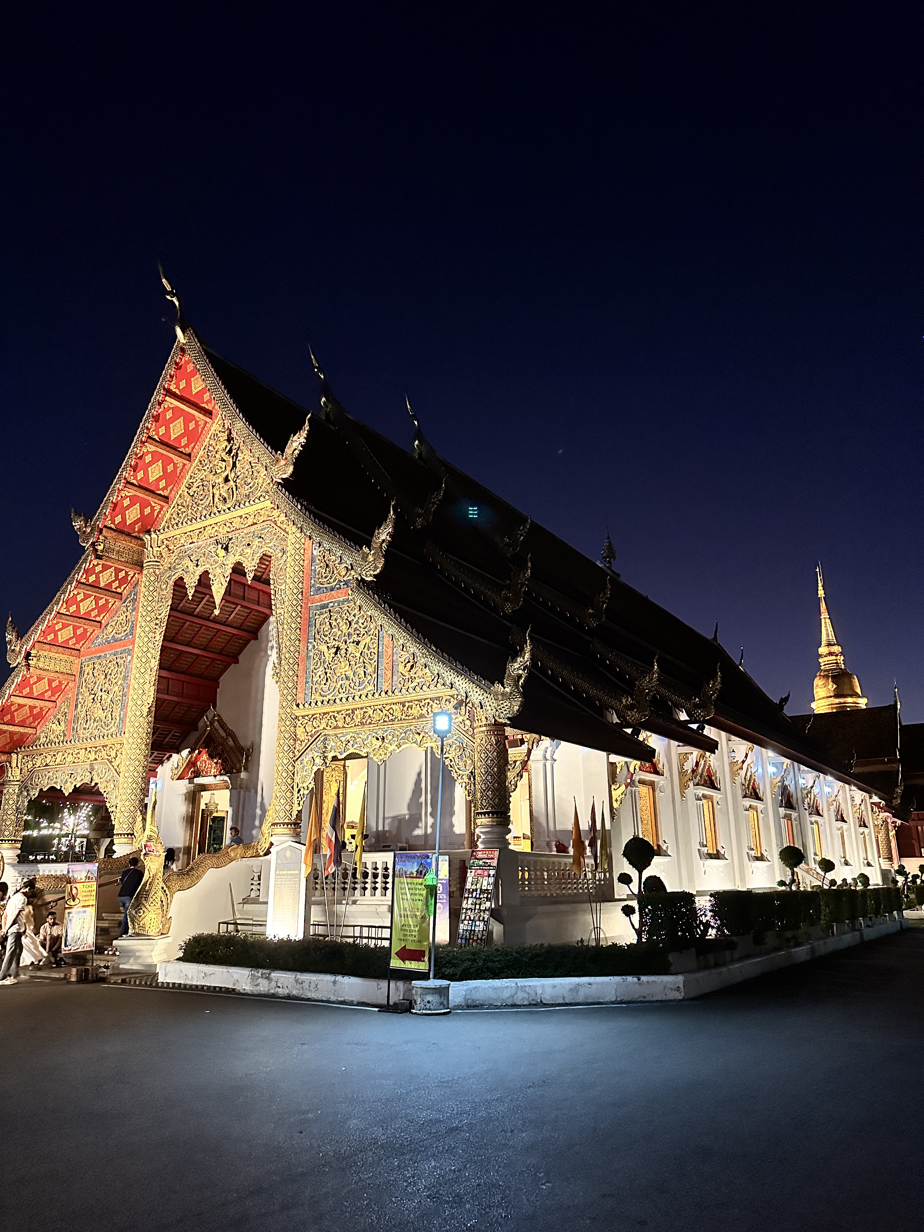 The long tiered roofline of Wat Phra Singh seen from the side at night with a golden chedi behind