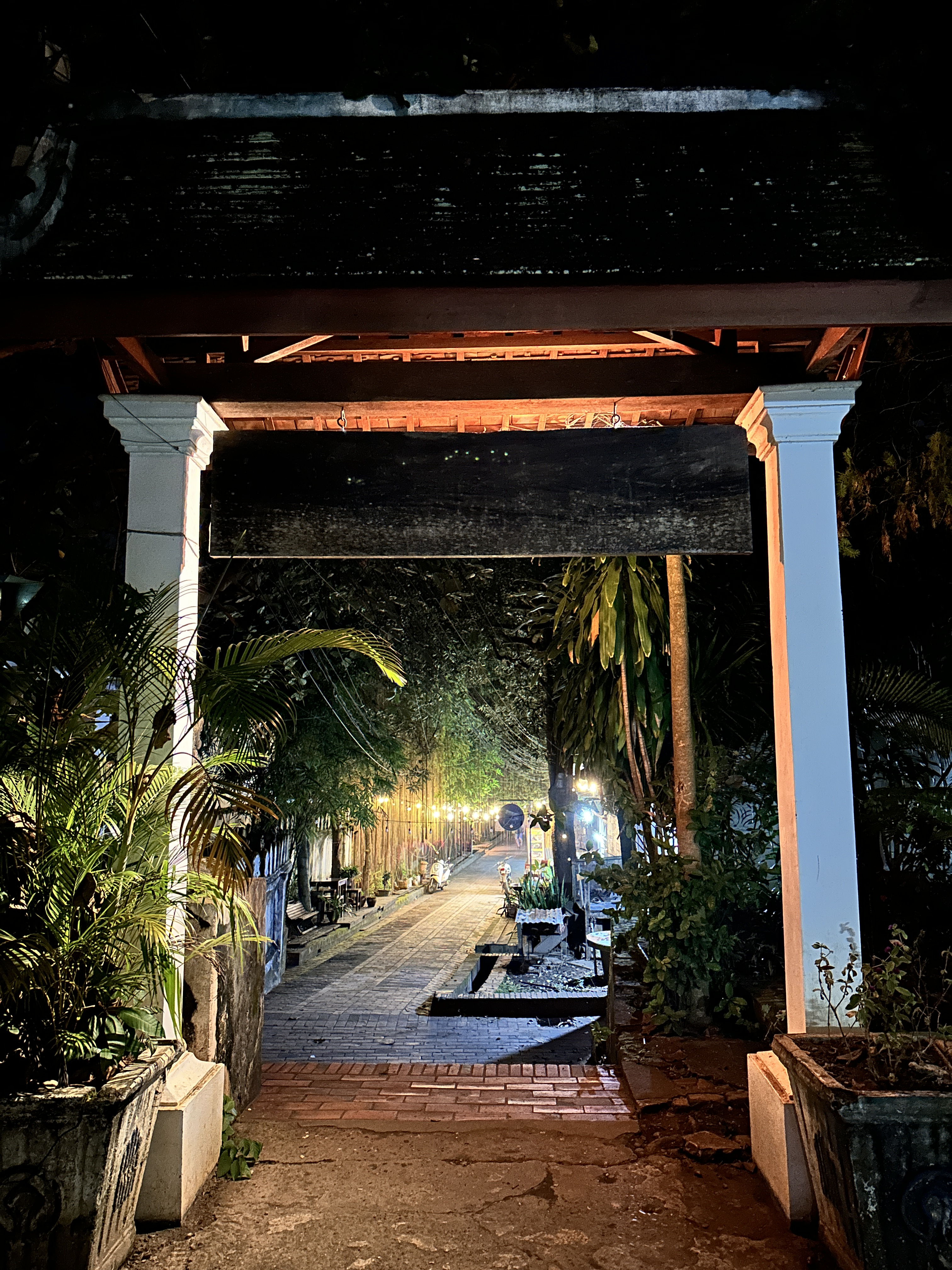 A lantern-lit lane in the old town of Luang Prabang at night, seen through a colonial gateway