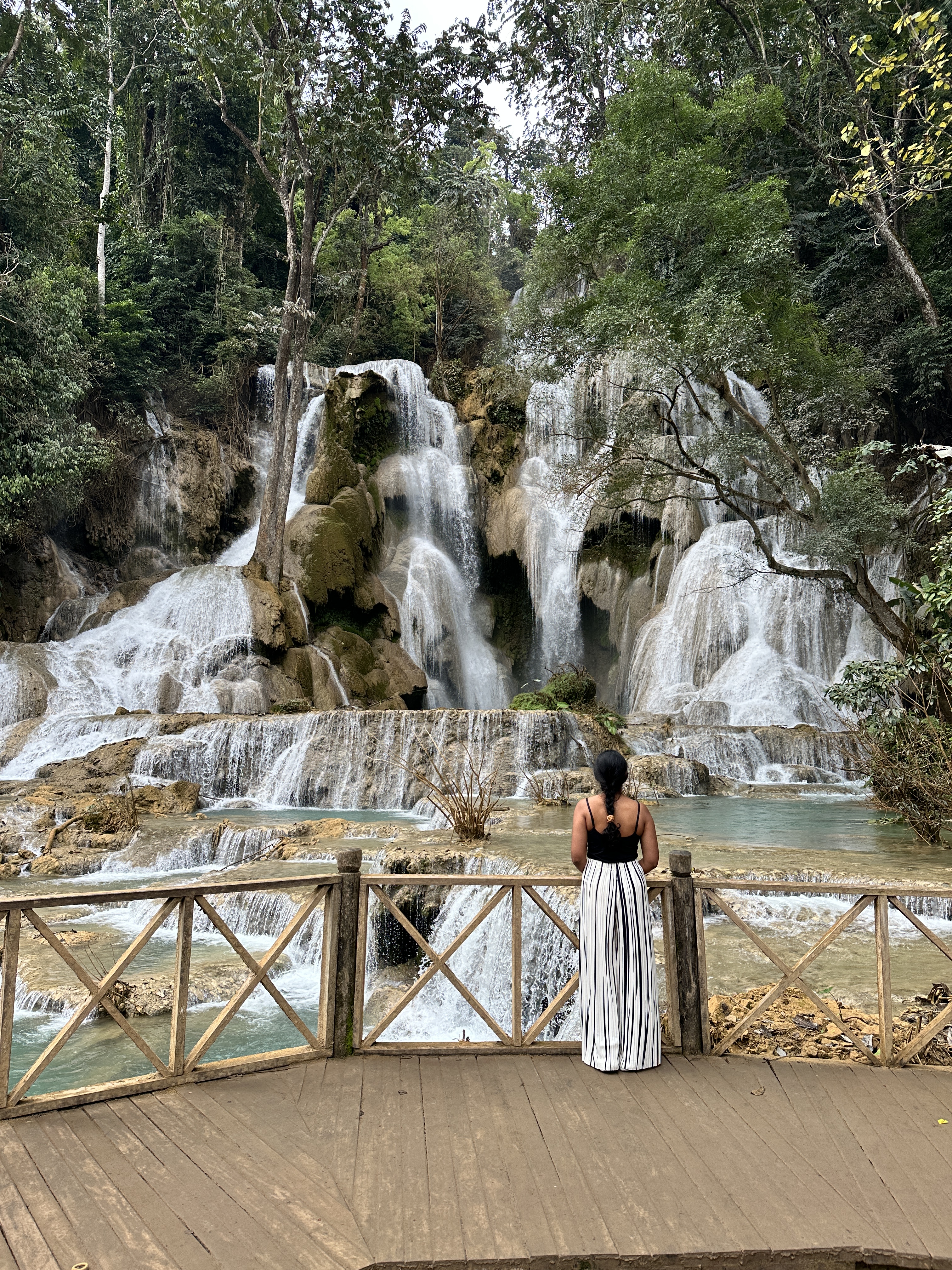 A woman looking at the turquoise tiered pools of Kuang Si Falls in the forest near Luang Prabang