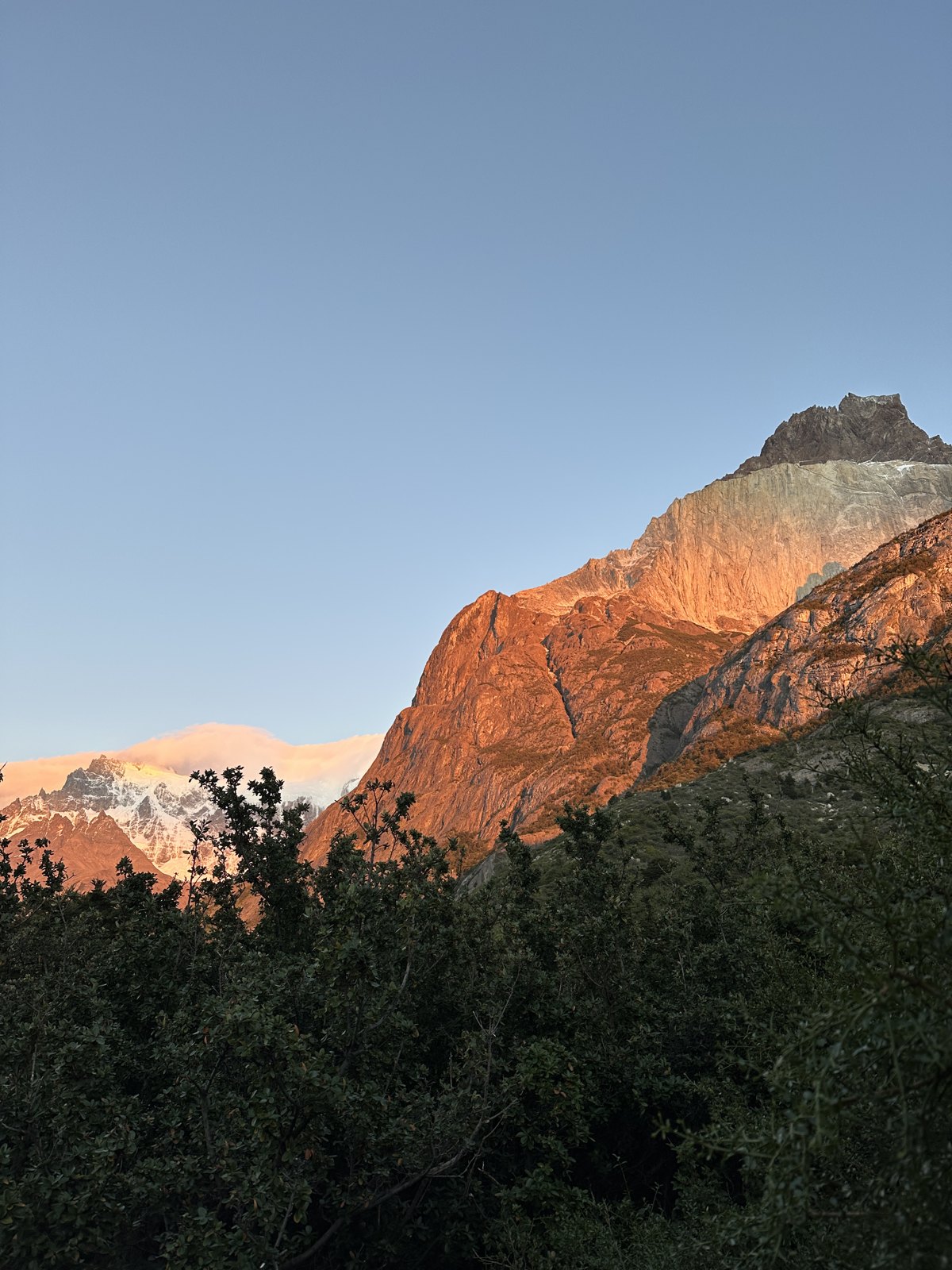 Early morning sun lighting an orange and grey mountain face above dark trees