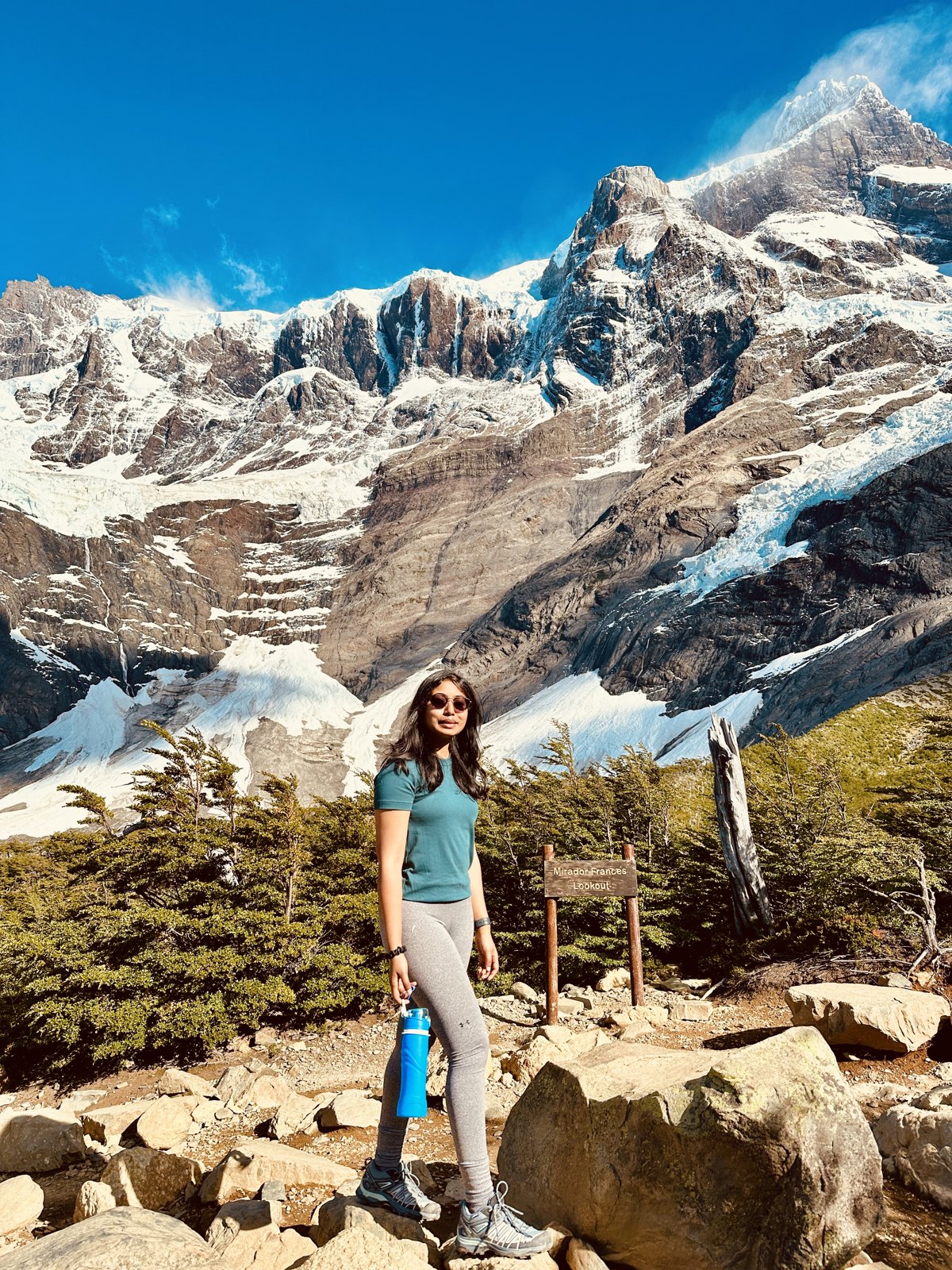 A woman standing on the trail in the French valley with an enormous wall of snow-covered peaks and hanging glaciers rising behind her