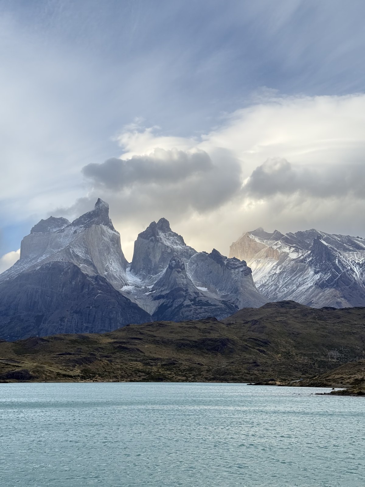 The Cuernos del Paine seen across the pale turquoise water of a lake from a boat, with cloud streaming off the peaks