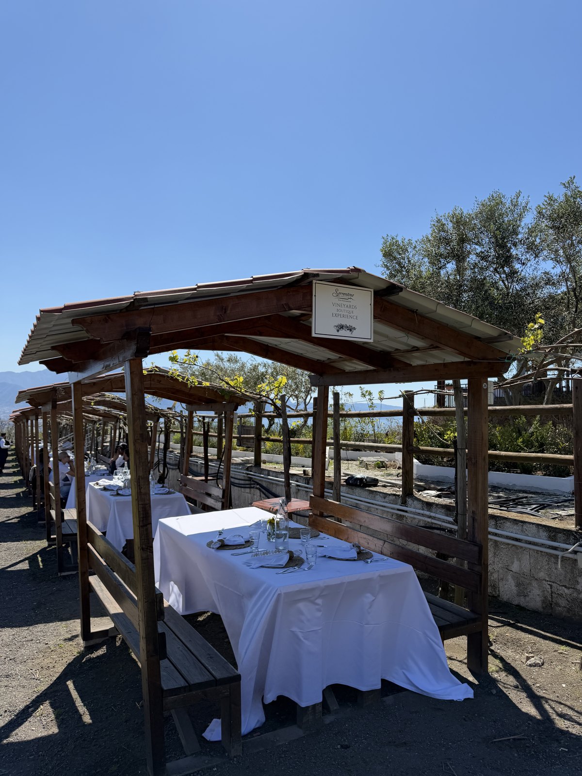 Outdoor tables under wooden pergolas set with white cloths in a vineyard on the mountainside