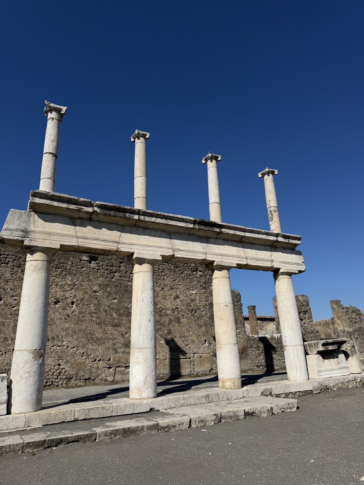 A double row of standing columns along the edge of the Pompeii forum against a deep blue sky