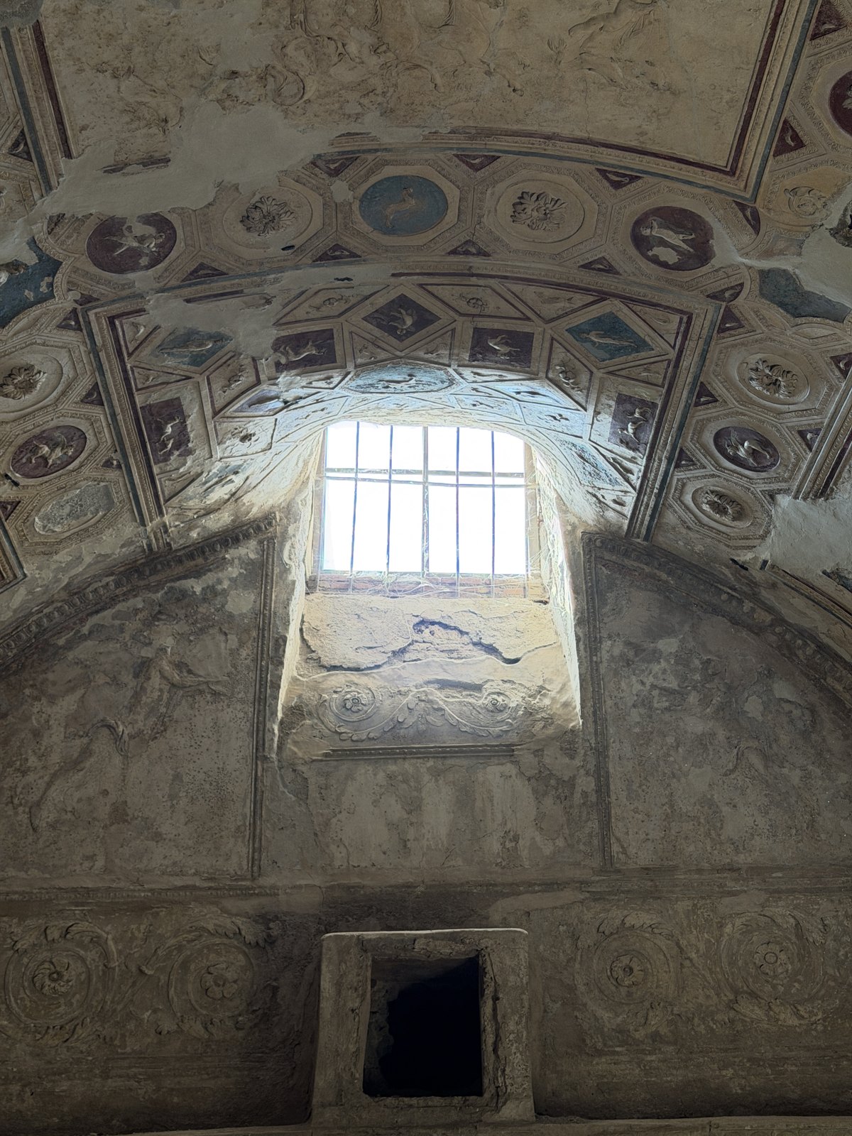 The vaulted ceiling of the Pompeii baths, covered in moulded stucco panels and figures around a barred skylight