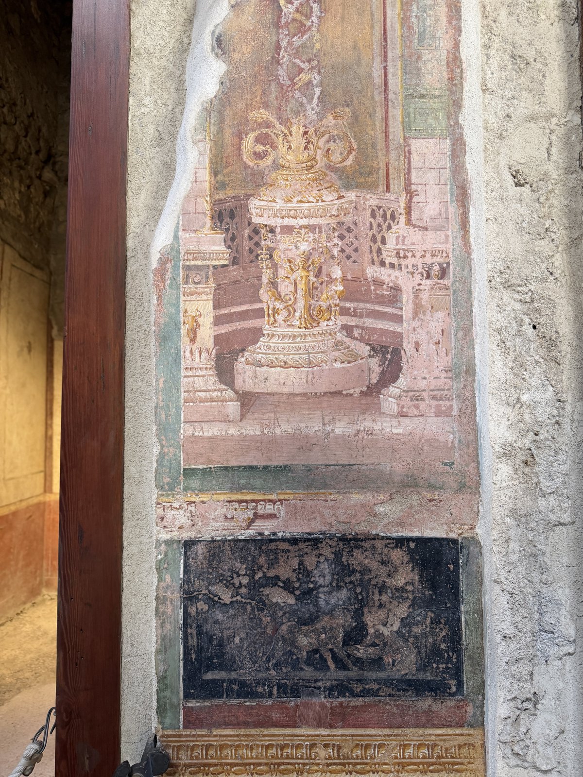 A detailed Pompeian fresco panel showing a delicate painted structure in pink and gold above a black frieze