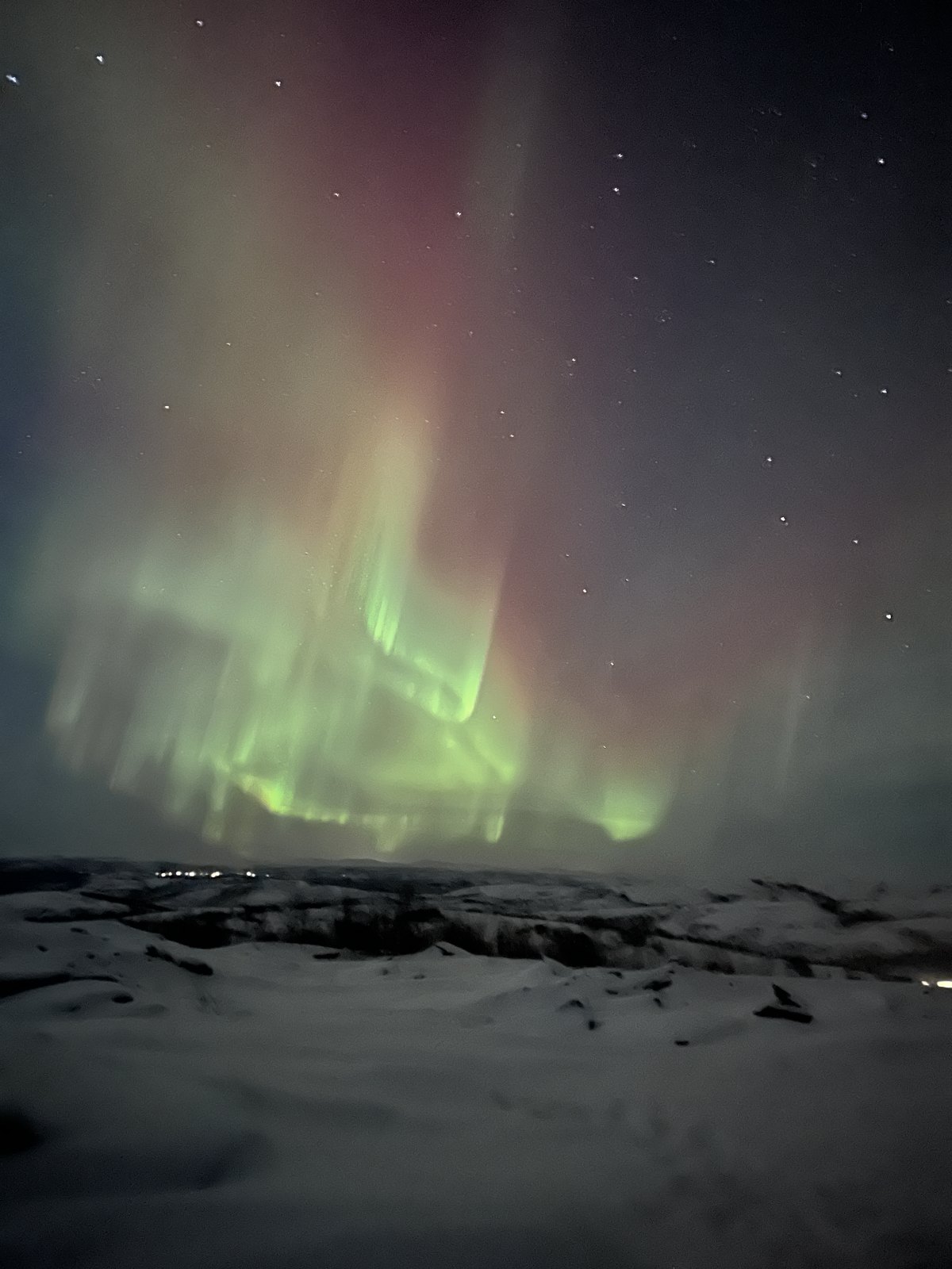 A wide band of green aurora with pink edges over a dark snow-covered landscape
