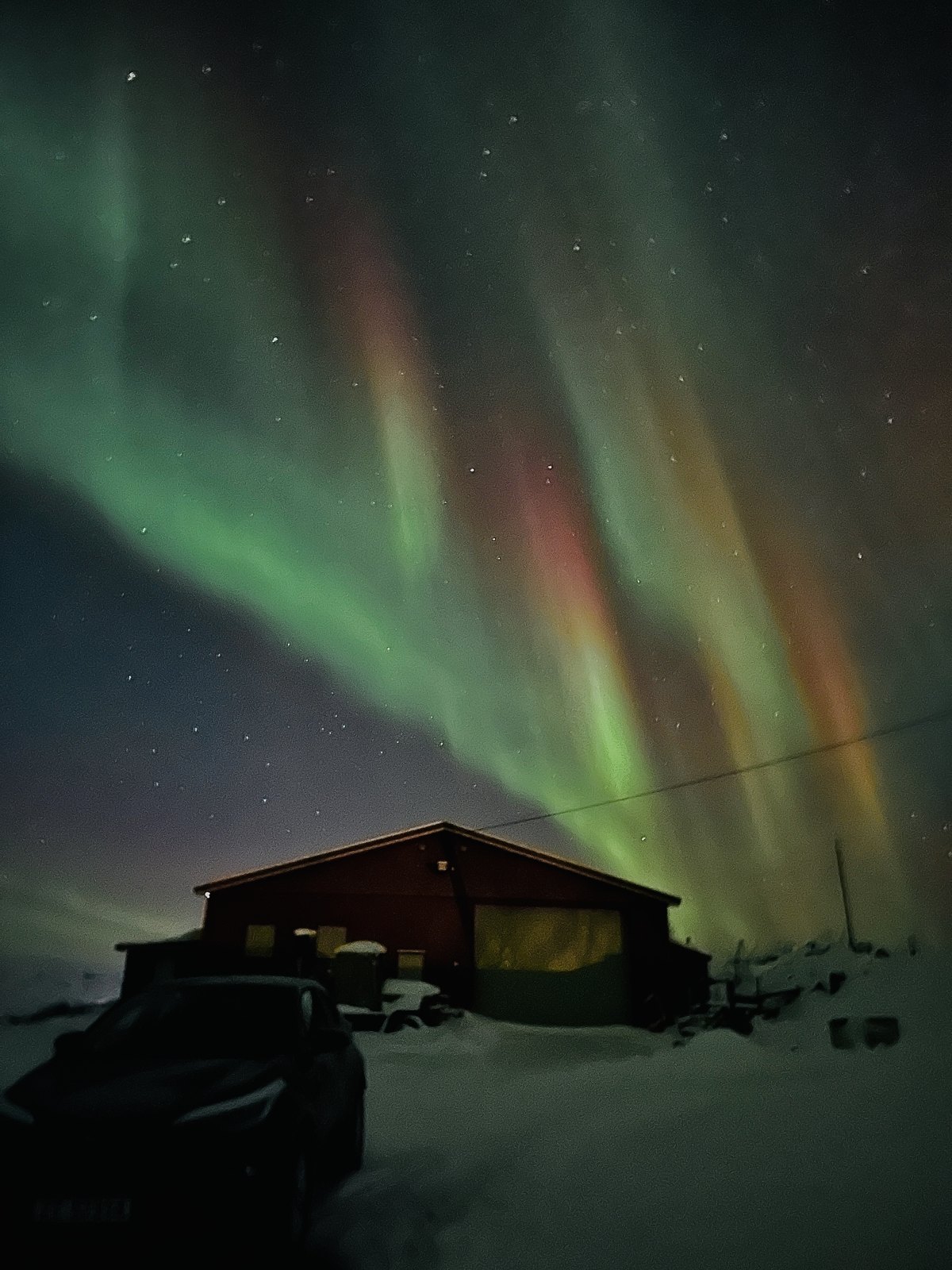 A wide green aurora filling the sky above an empty snowfield with a low horizon