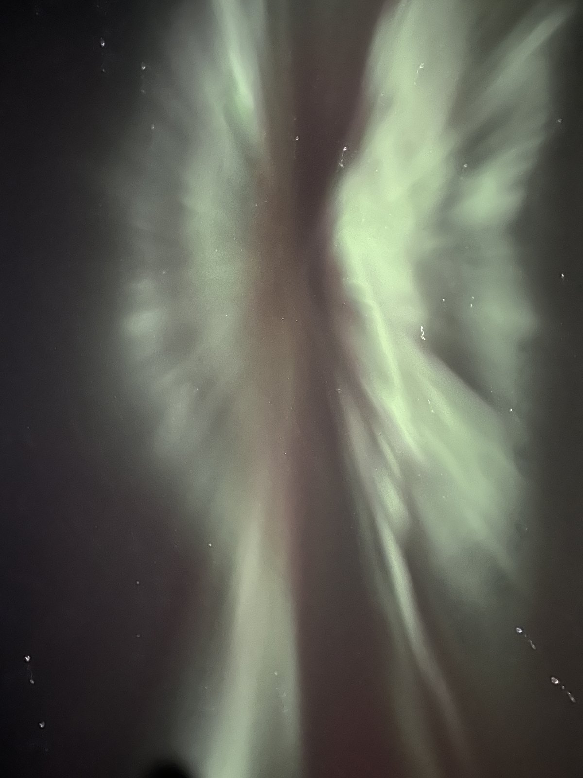 A bright aurora corona directly overhead, with rays radiating out from a central point across a dark sky
