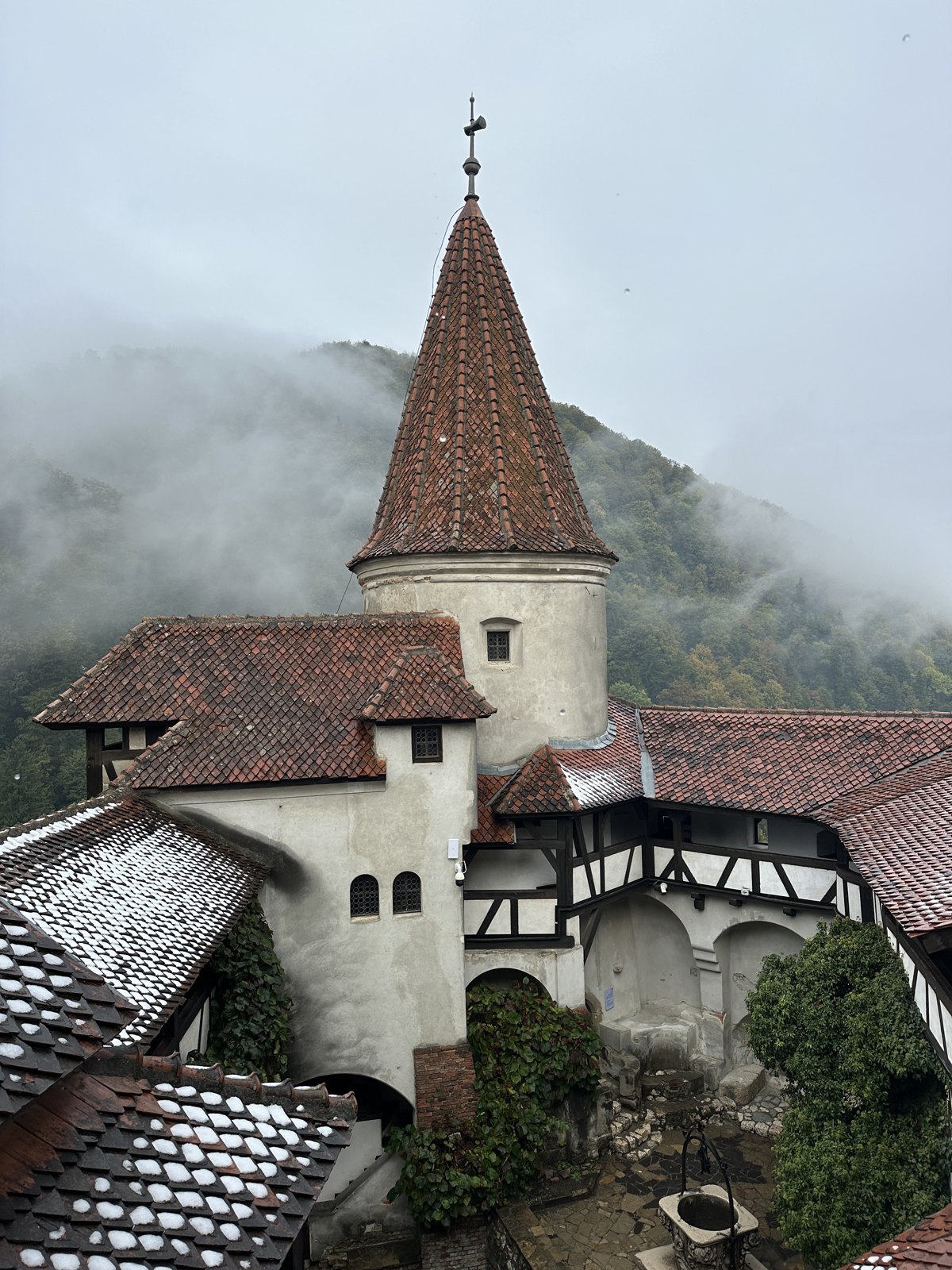 The red-tiled turret and white walls of Bran Castle with forested hills and low cloud behind