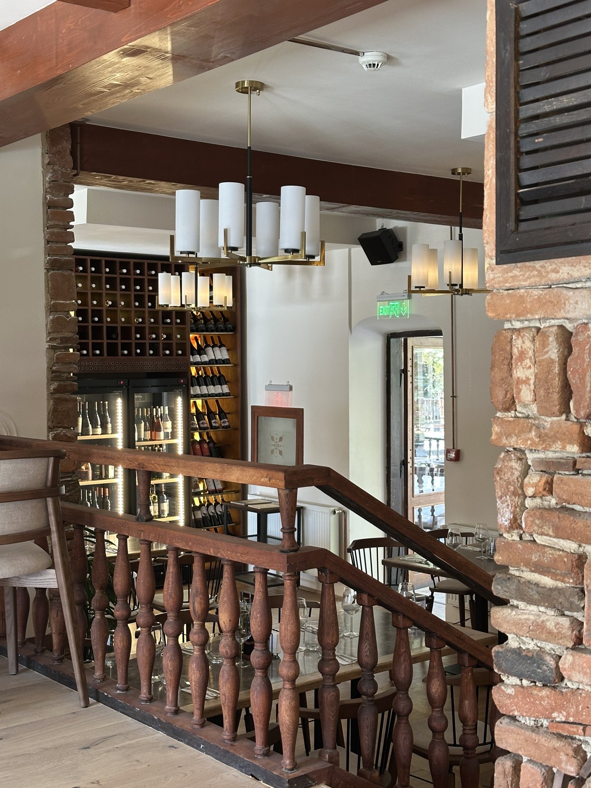 The interior of a restaurant with exposed brick, wooden beams, a wine rack and a carved wooden staircase