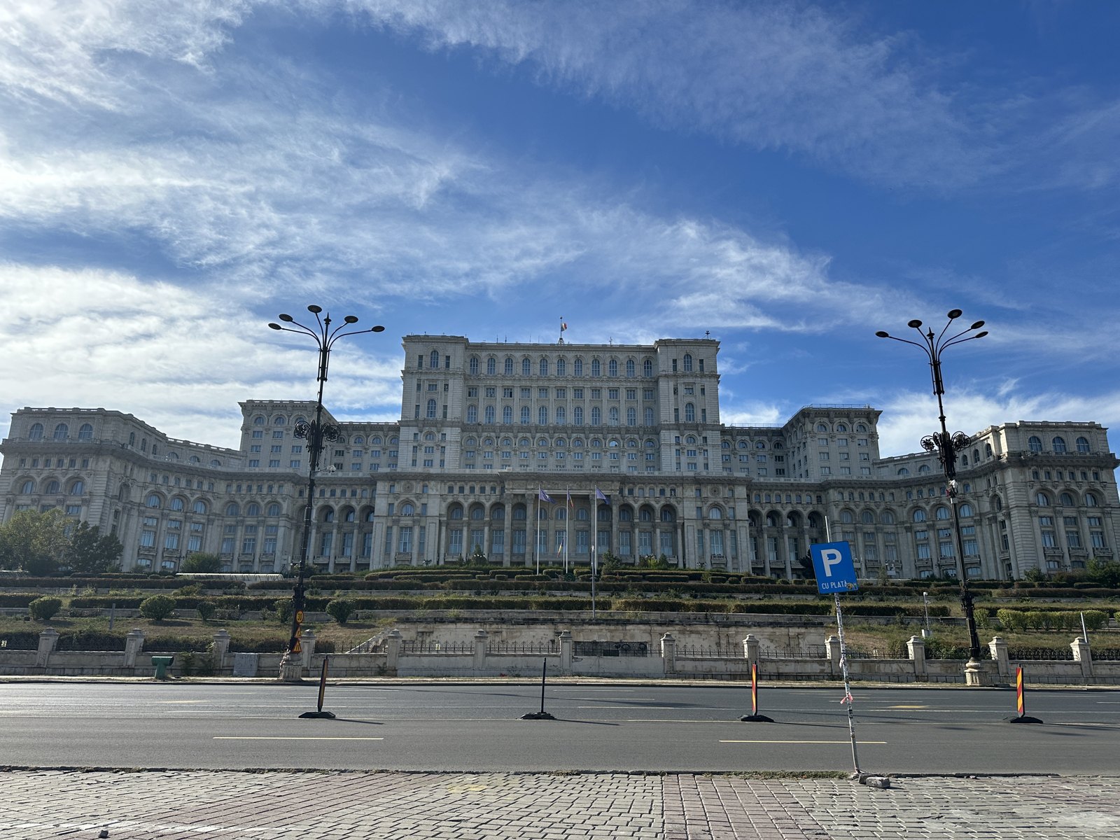 The vast white facade of the Palace of the Parliament in Bucharest under a blue sky, seen from across a wide empty boulevard