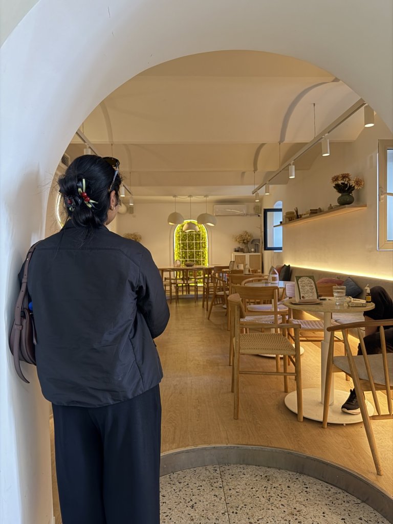 A woman looking into a calm, light-filled café with an arched entrance and wooden tables