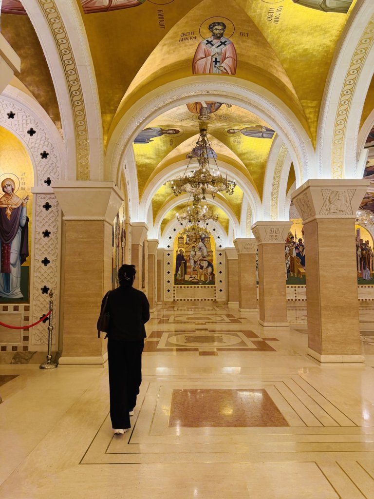 A woman walking through the golden, painted crypt of the Church of Saint Sava