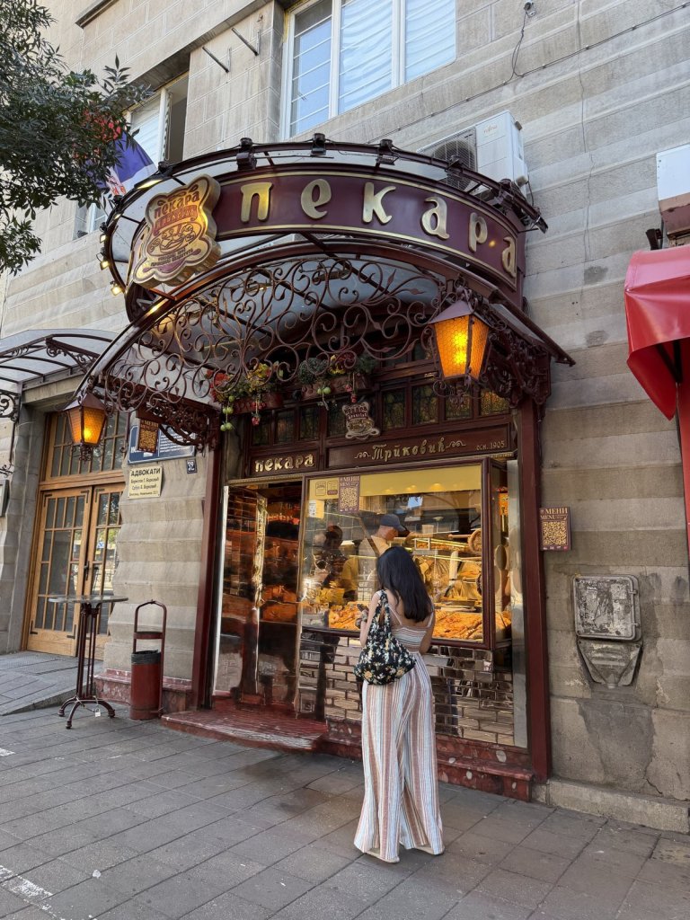 A woman looking into the window of a traditional Serbian bakery with an ornate iron canopy
