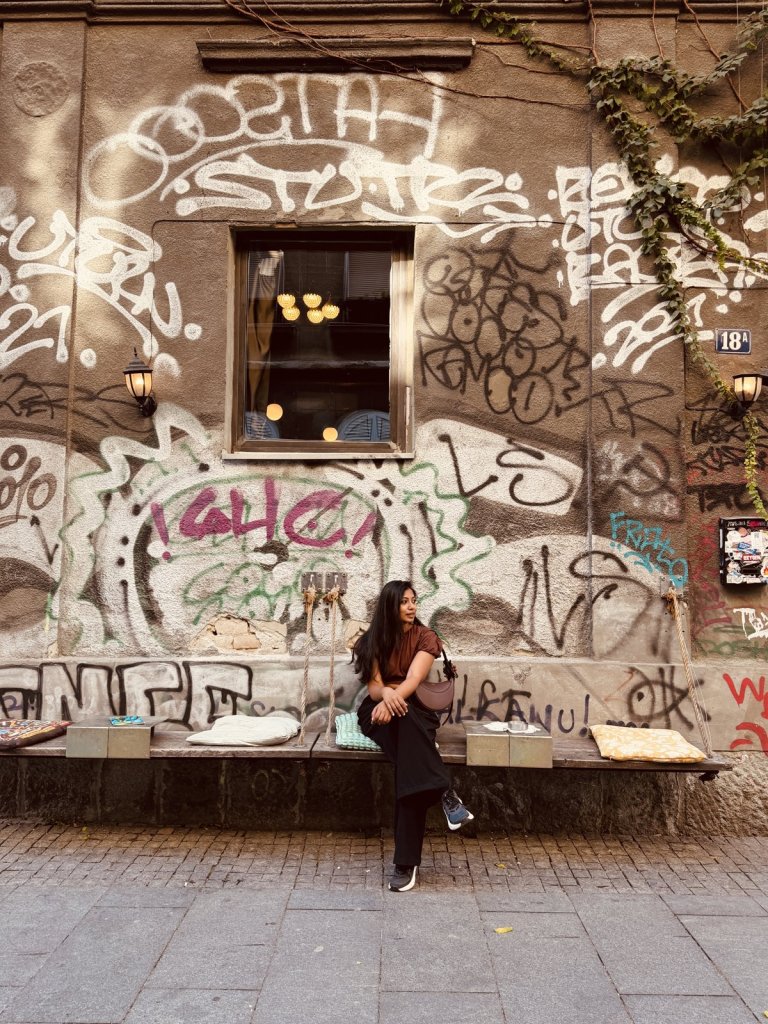 A woman sitting on a bench in front of a heavily graffitied old building